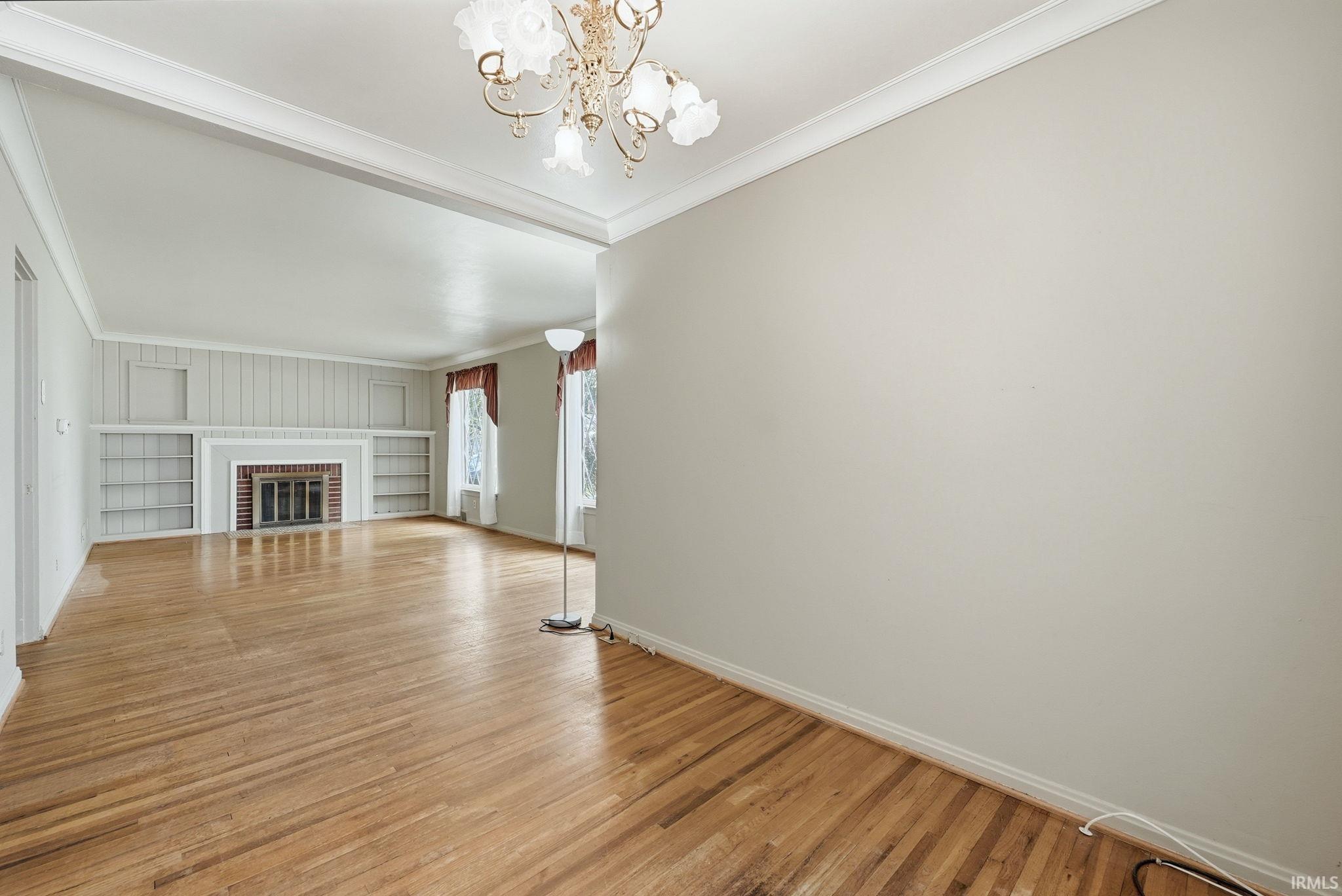 Spacious room featuring wood-finish flooring, an ornate chandelier, and crown molding