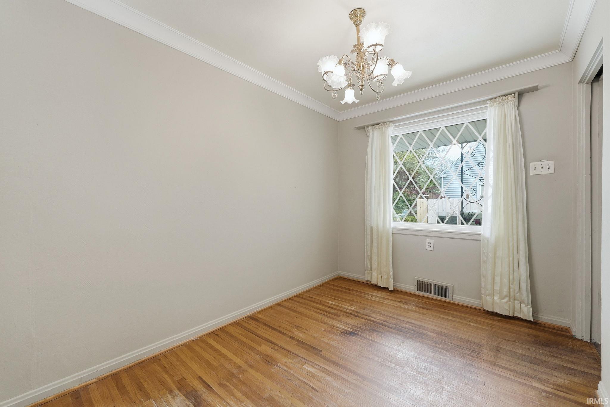 Room featuring wood-finish flooring, a decorative chandelier, crown molding, baseboards, and a window with a diamond-patterned grid
