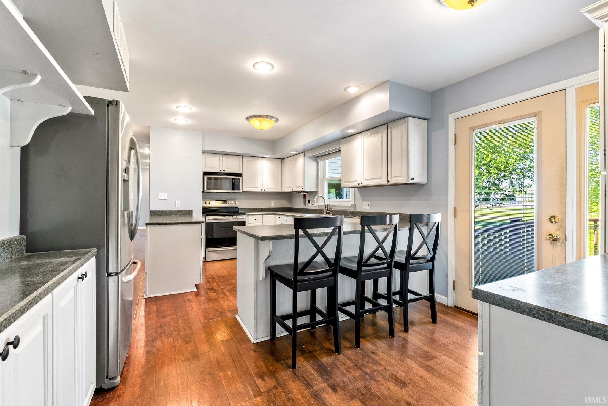 Kitchen featuring wood-finish flooring, white cabinetry, dark countertops, a central island with seating, and stainless steel appliances