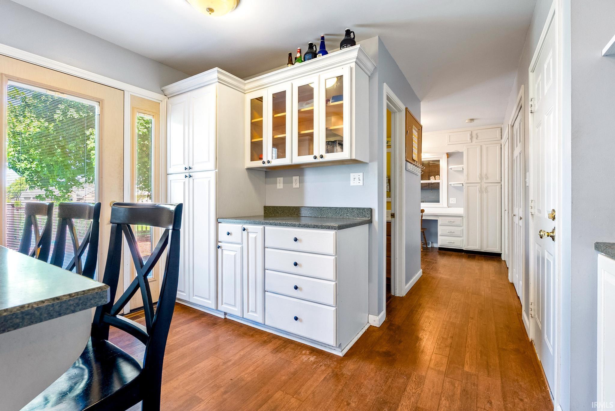 Kitchen area featuring white cabinetry, glass-front upper cabinets, and dark countertops