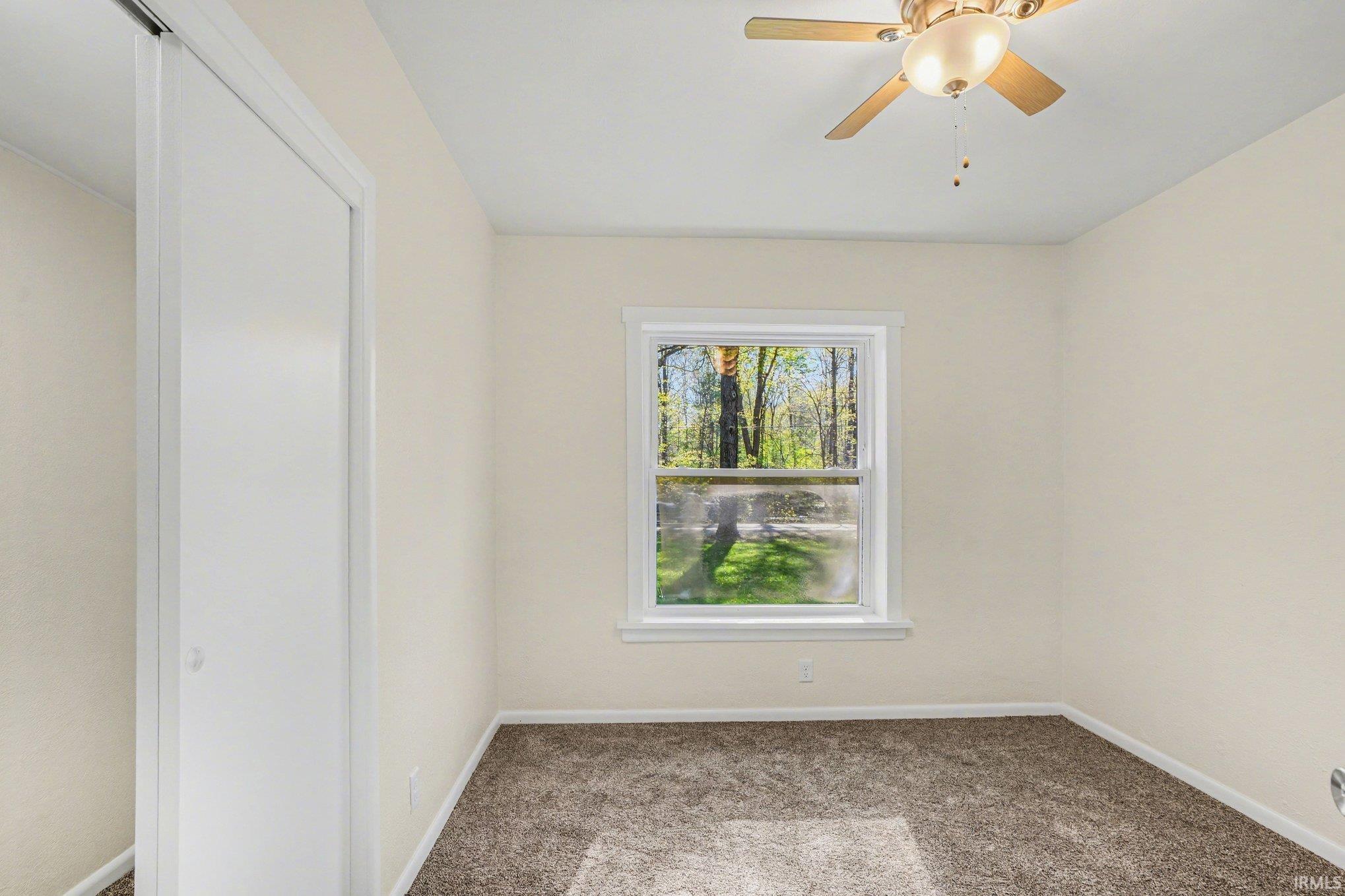 Carpeted room with a ceiling fan light fixture, a window with white trim, and a bi-fold closet door
