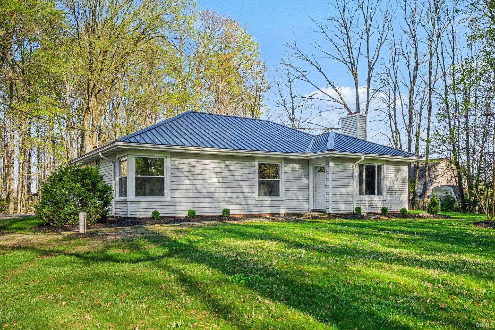 Single-story residence featuring a blue metal roof, light-colored horizontal siding, and a prominent chimney