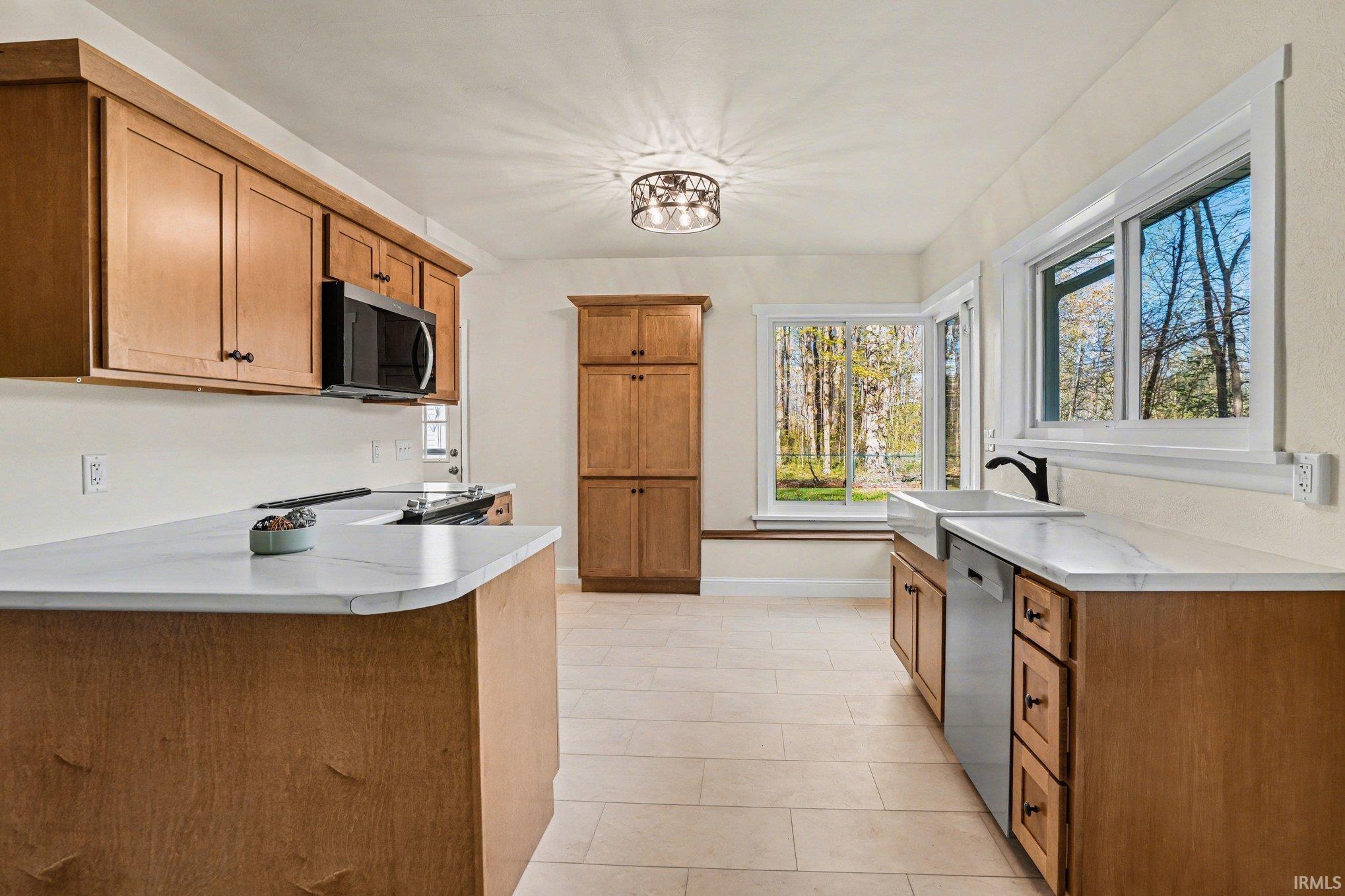 Kitchen featuring wood cabinetry, white countertops, stainless steel appliances, a farmhouse sink with a black faucet, and tiled flooring