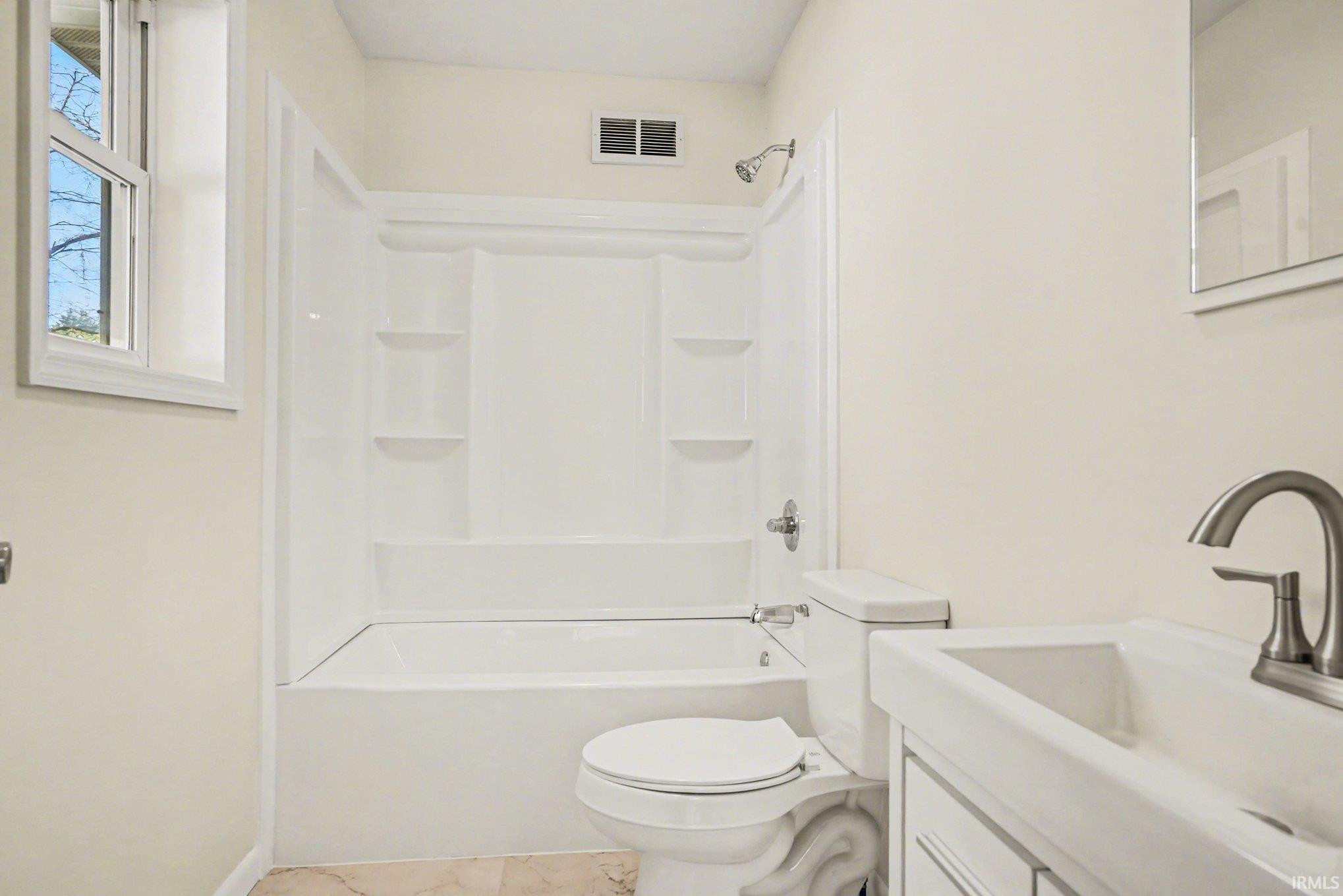 Bathroom featuring a white bathtub/shower combination with integrated shelving, a white toilet, and a white vanity with a rectangular sink and brushed nickel faucet