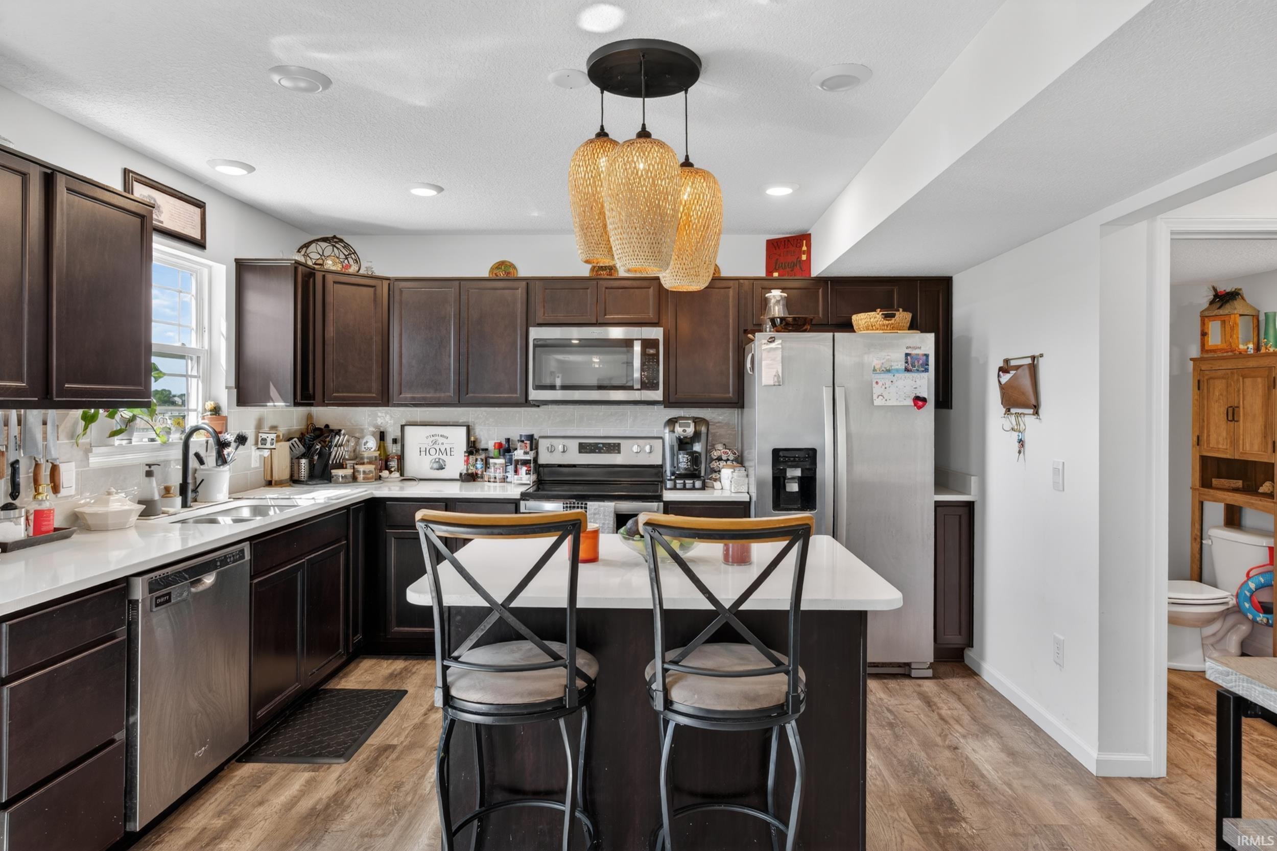 Kitchen featuring dark wood cabinetry, white countertops, stainless steel appliances, and wood-finish flooring