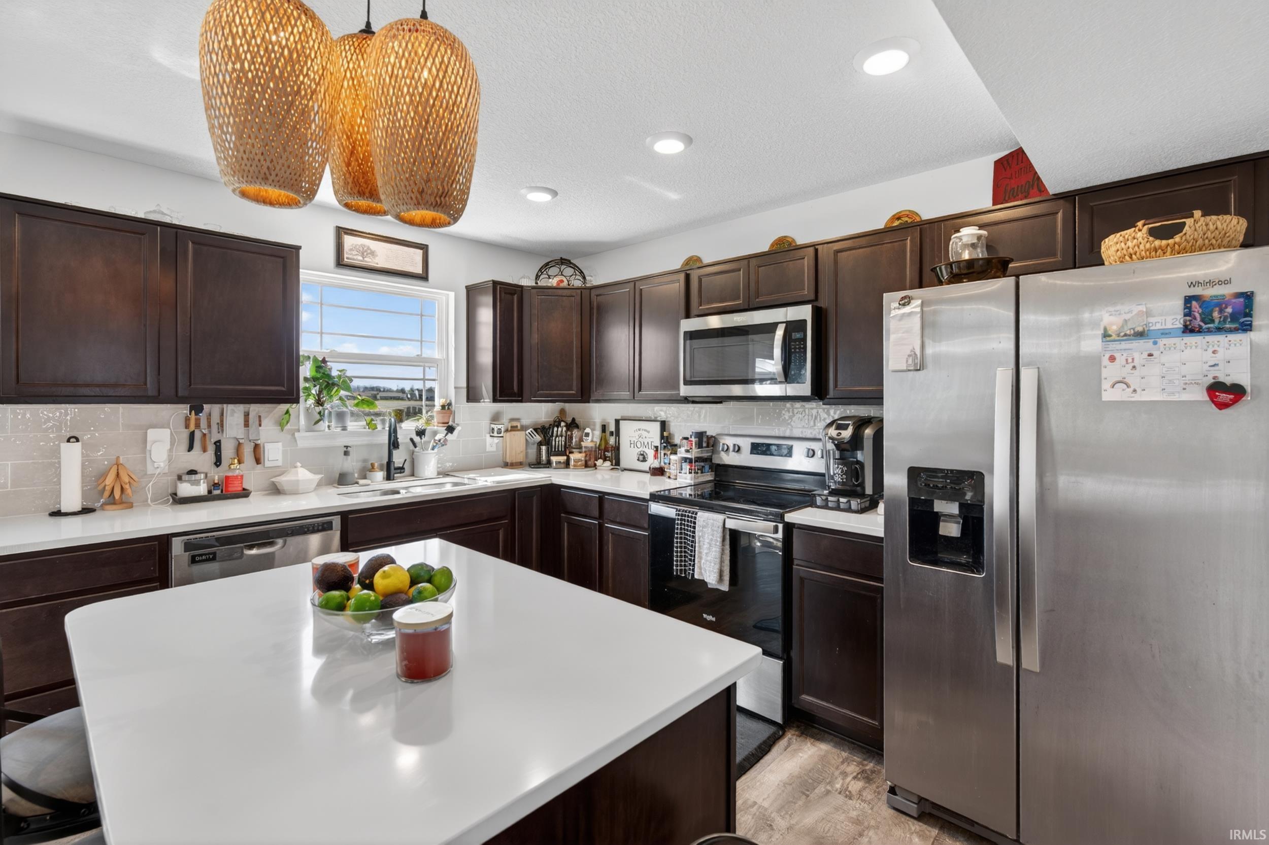 Open-concept kitchen featuring dark wood cabinetry, stainless steel appliances, a center island with a white countertop, recessed lighting, and wood-finish flooring