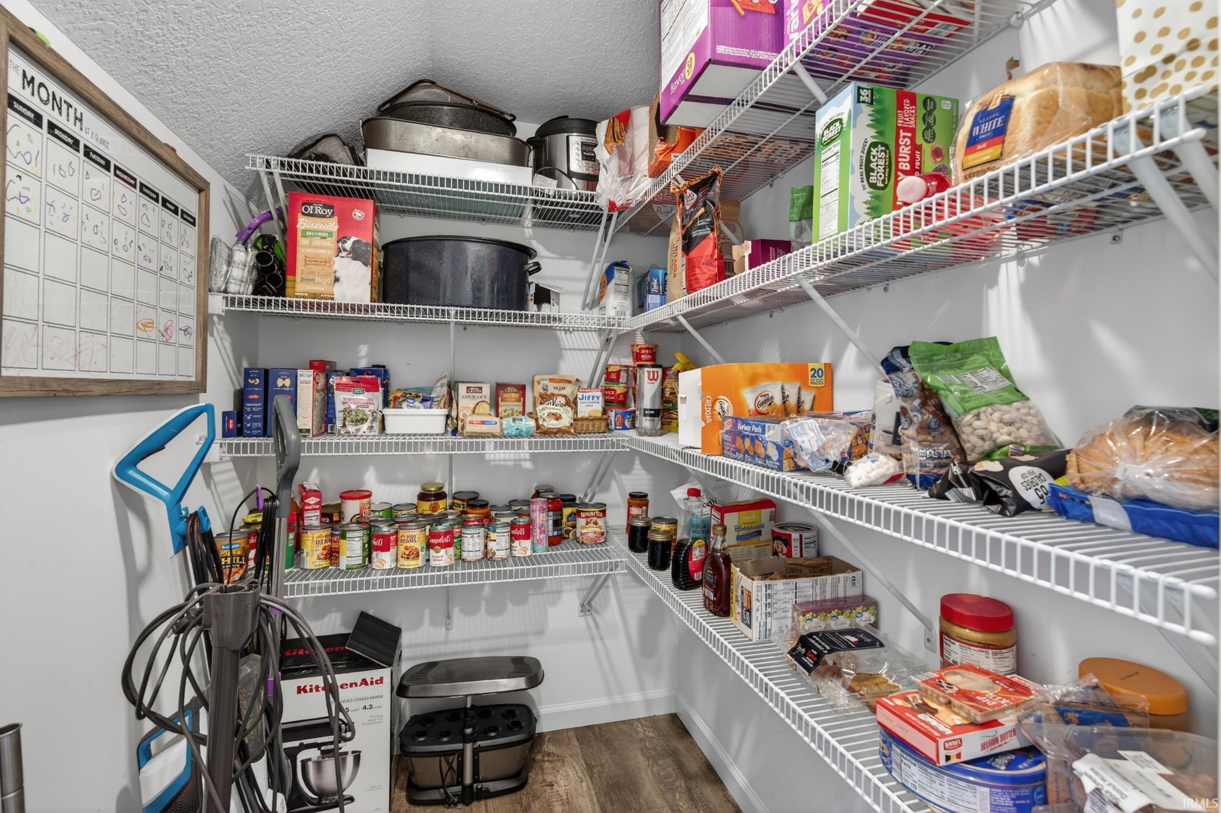 Walk-in pantry featuring wire shelving, white walls, and wood-finish flooring