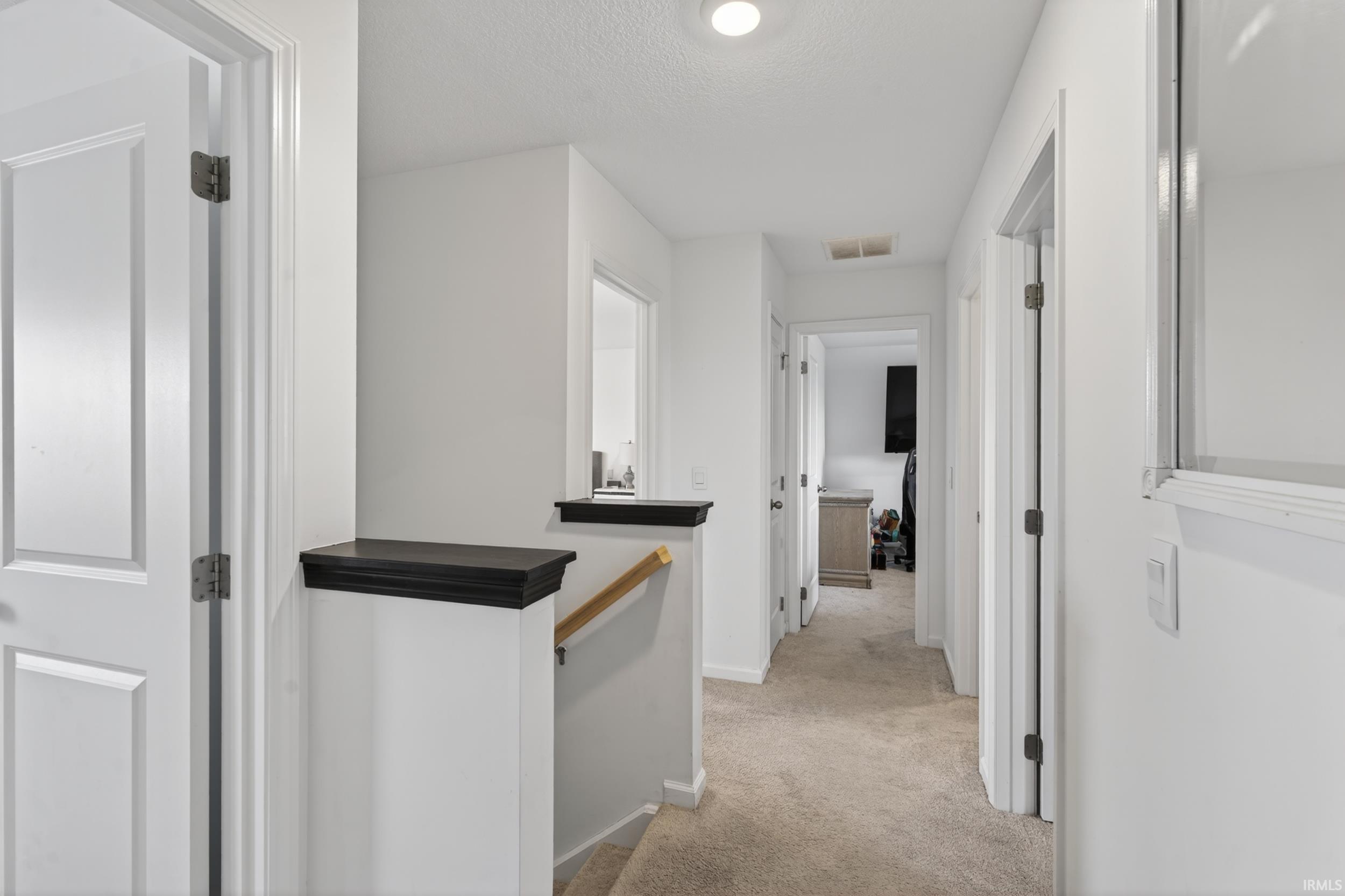 Hallway featuring neutral carpet flooring, recessed lighting, white walls, and a staircase with a wood handrail and dark cap