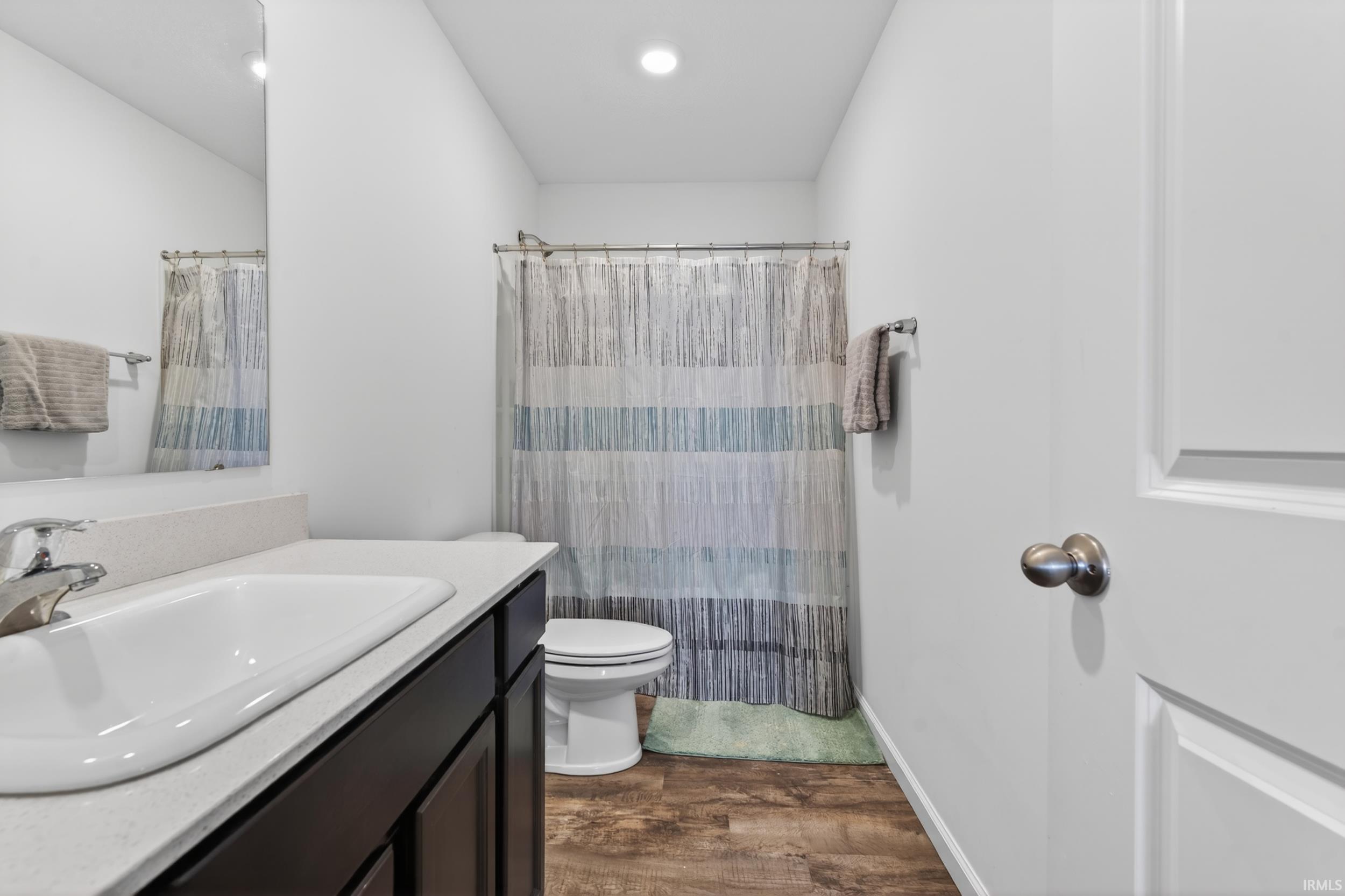 Full bathroom featuring a dark wood-finish vanity with an integrated sink and light-toned countertop, a shower-tub combination, and wood-finish flooring