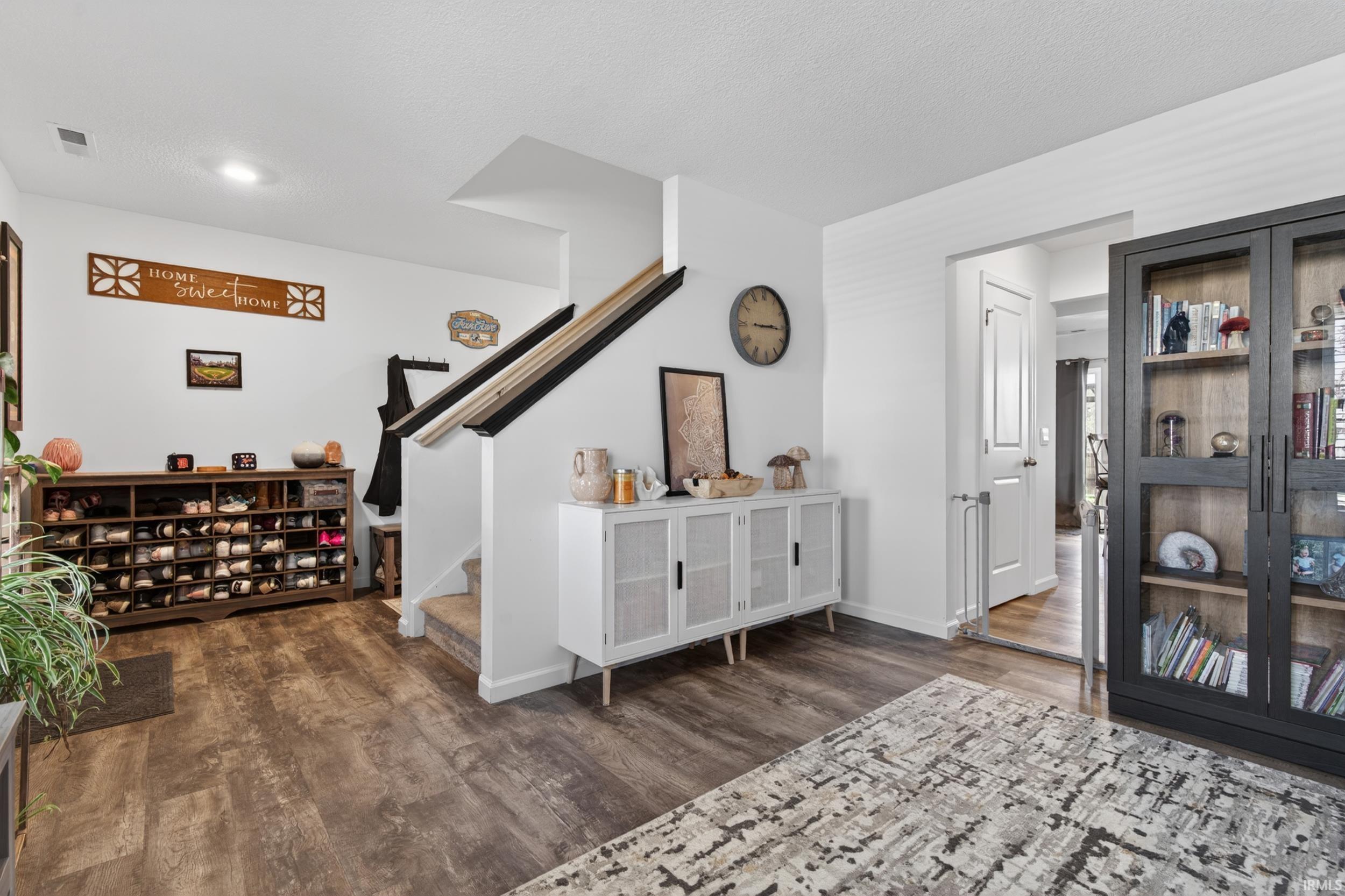 Entryway featuring wood-finish flooring, a carpeted staircase with a black handrail, and white walls