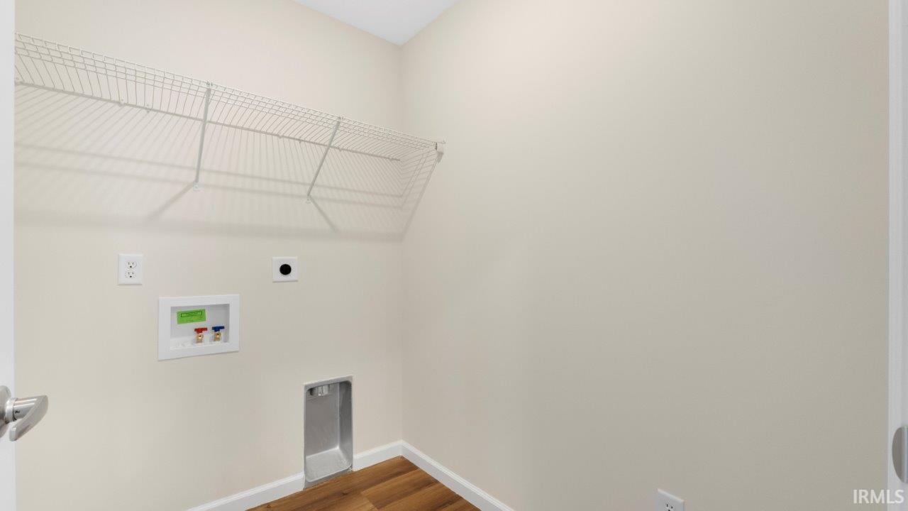 Dedicated laundry area featuring a wire storage shelf, recessed plumbing hookups, electrical outlets, and wood-finish flooring
