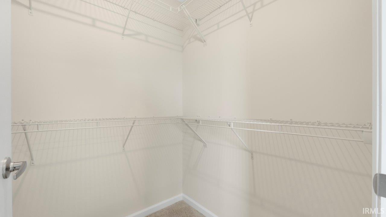 Walk-in closet with beige wall paint, white wire shelving, wall-to-wall carpeting, and brushed nickel hardware