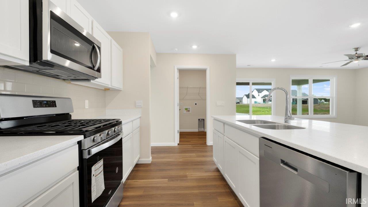 Kitchen featuring white cabinetry, stainless steel appliances, a center island with an undermount sink, and wood-finish flooring