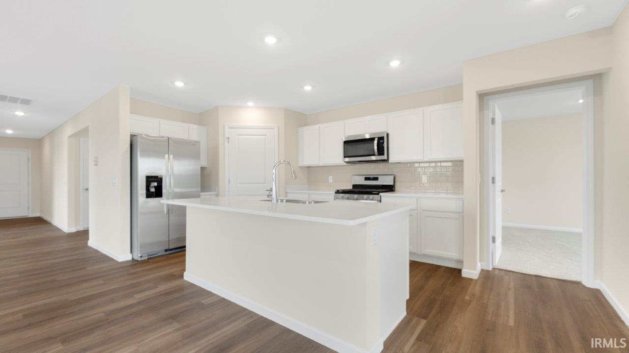 Modern kitchen featuring a central island with an undermount sink, white cabinetry, stainless steel appliances, and wood-finish flooring