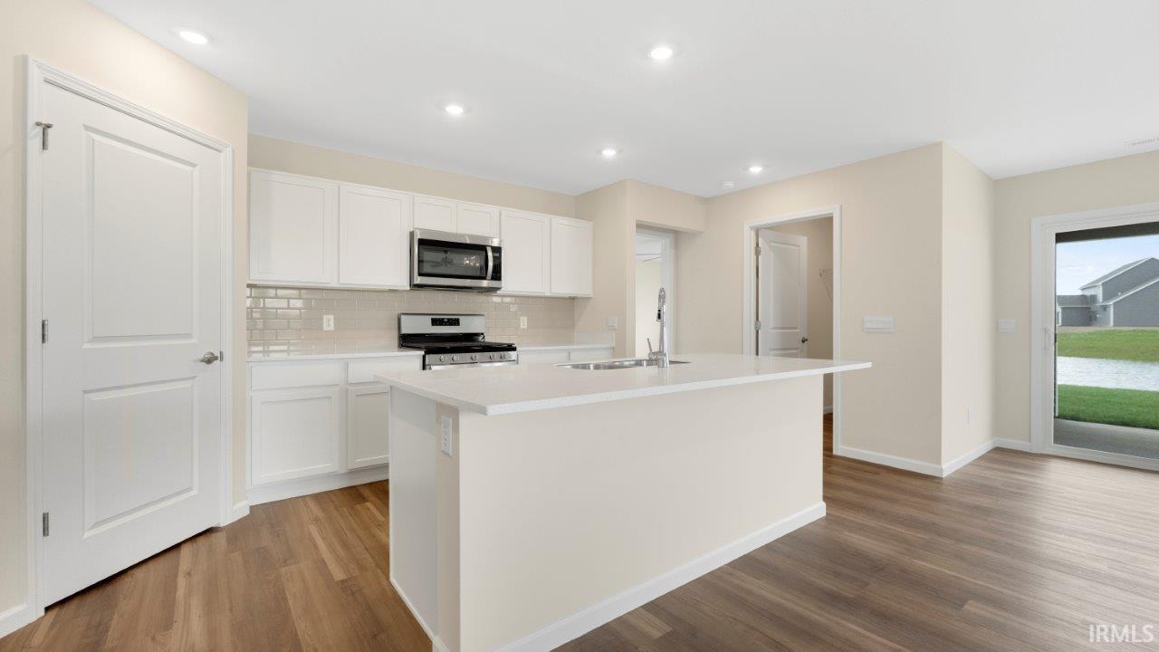 Kitchen featuring white cabinetry, light-toned countertop island with sink, stainless steel appliances, and wood-finish flooring