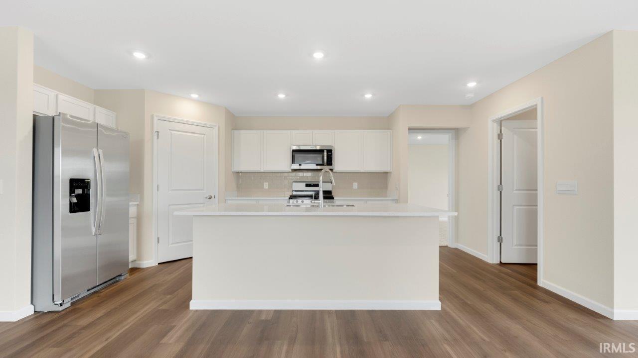 Modern kitchen featuring a central island with a sink, stainless steel appliances, recessed lighting, wood-finish flooring, and light-toned cabinetry