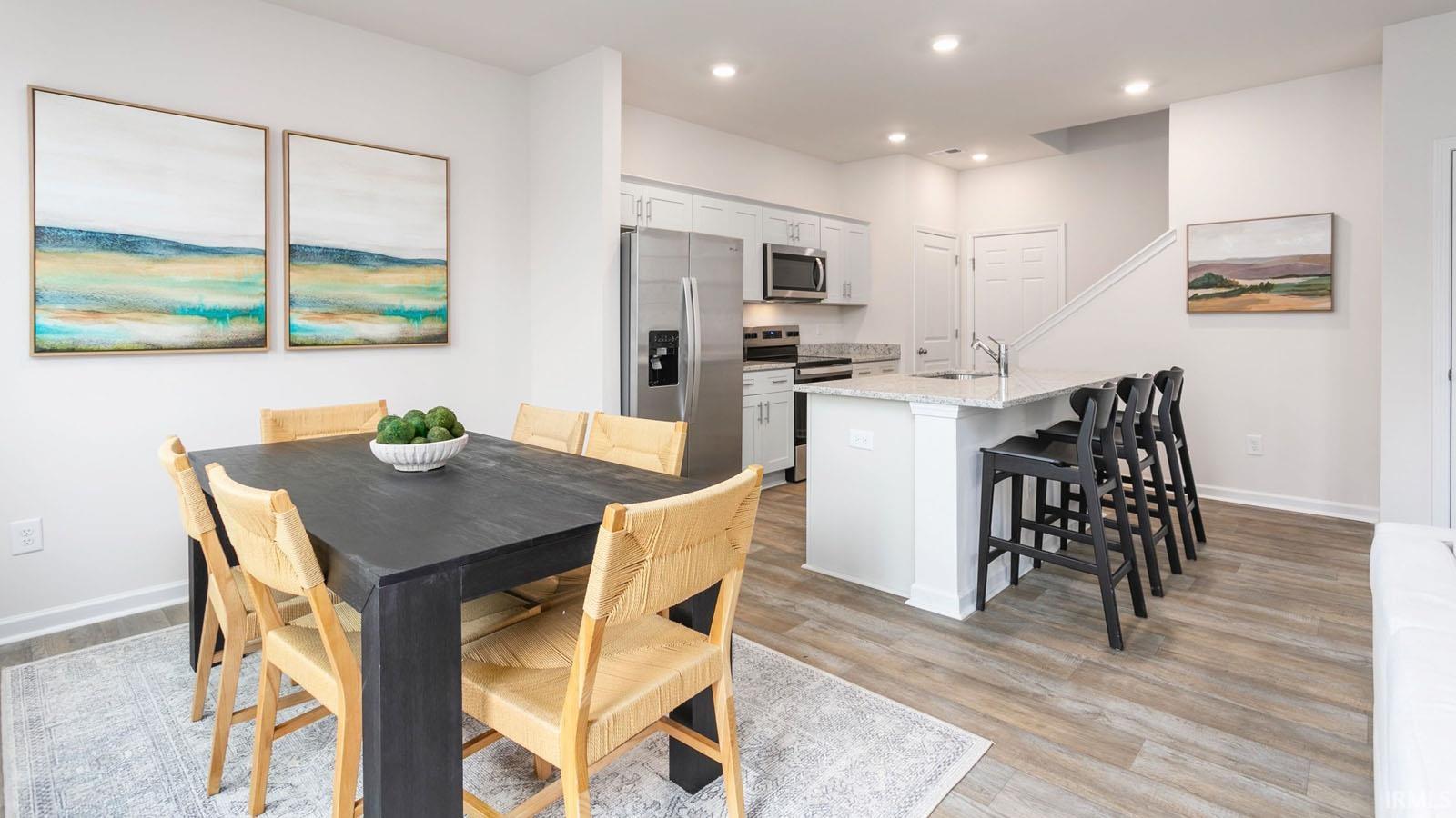 Open-concept dining area and kitchen featuring wood-finish flooring, recessed lighting, white cabinetry, and stainless steel appliances