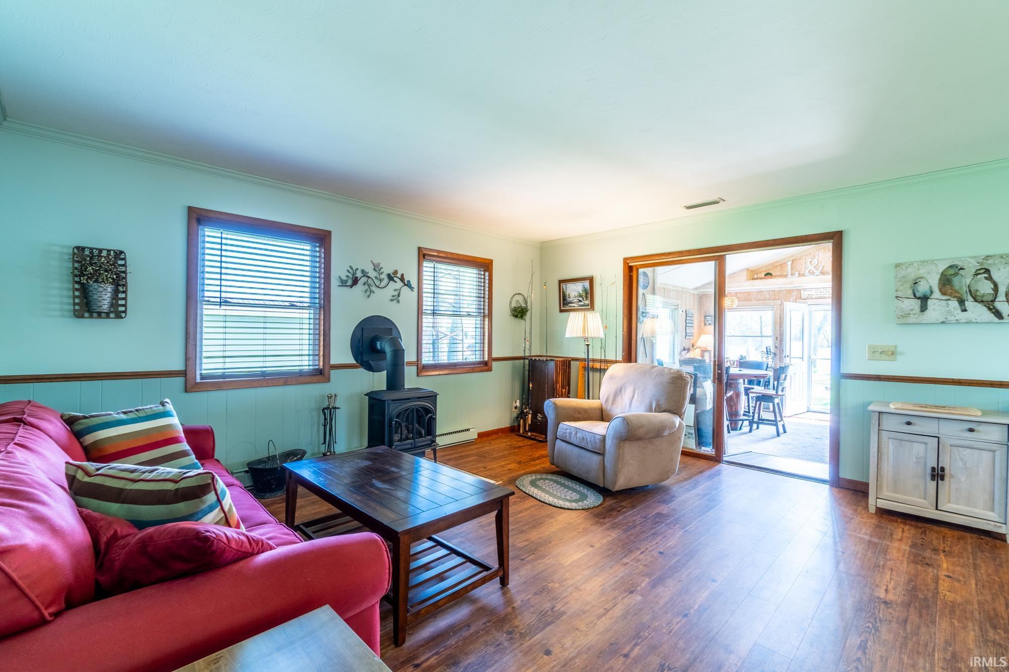 Interior living space featuring wood-finish flooring, light green walls with wainscoting, and wood-framed windows with blinds
