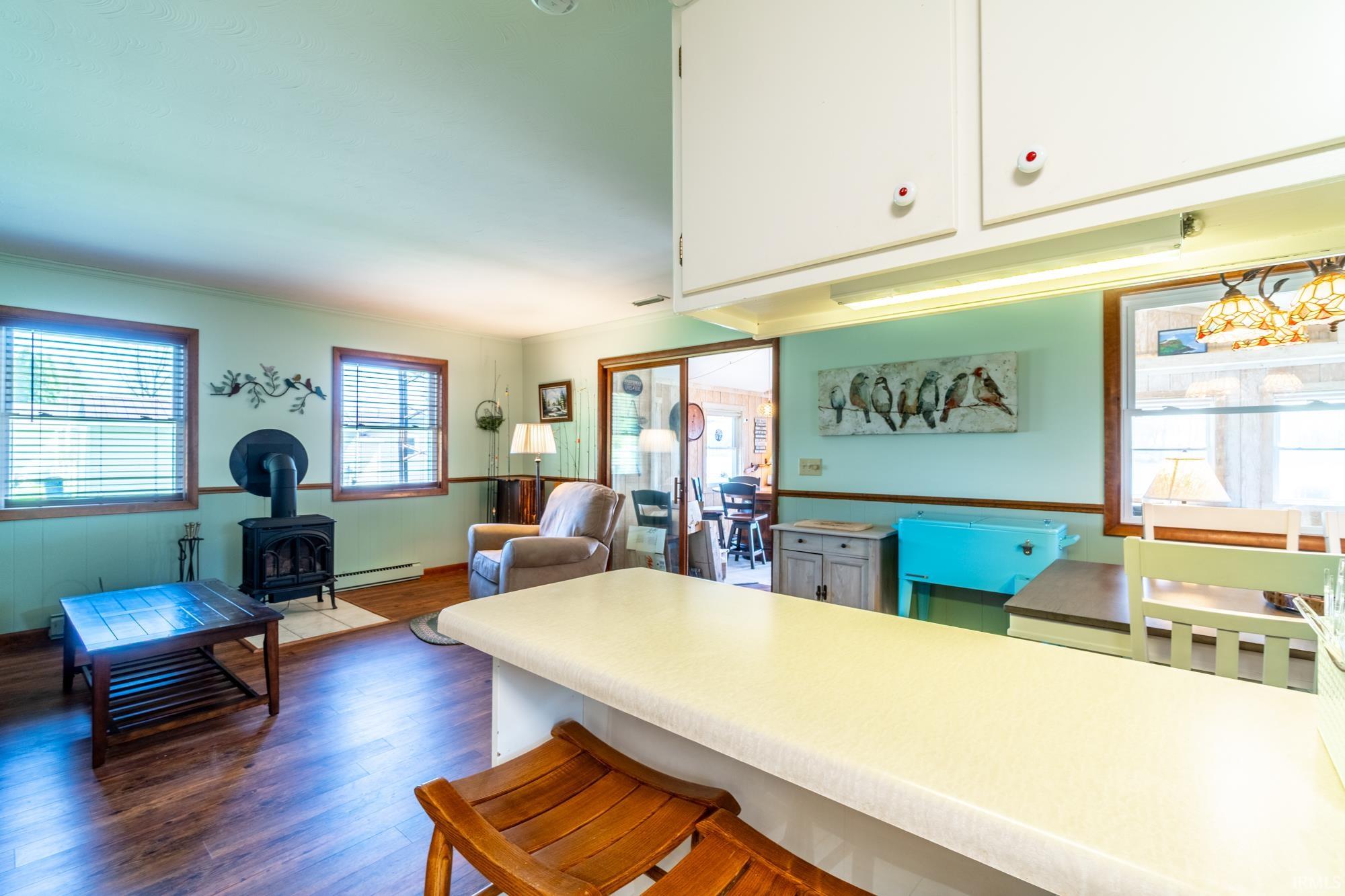 Open-concept living area with wood-finish flooring, multiple windows, and a black wood-burning stove on a light-colored hearth