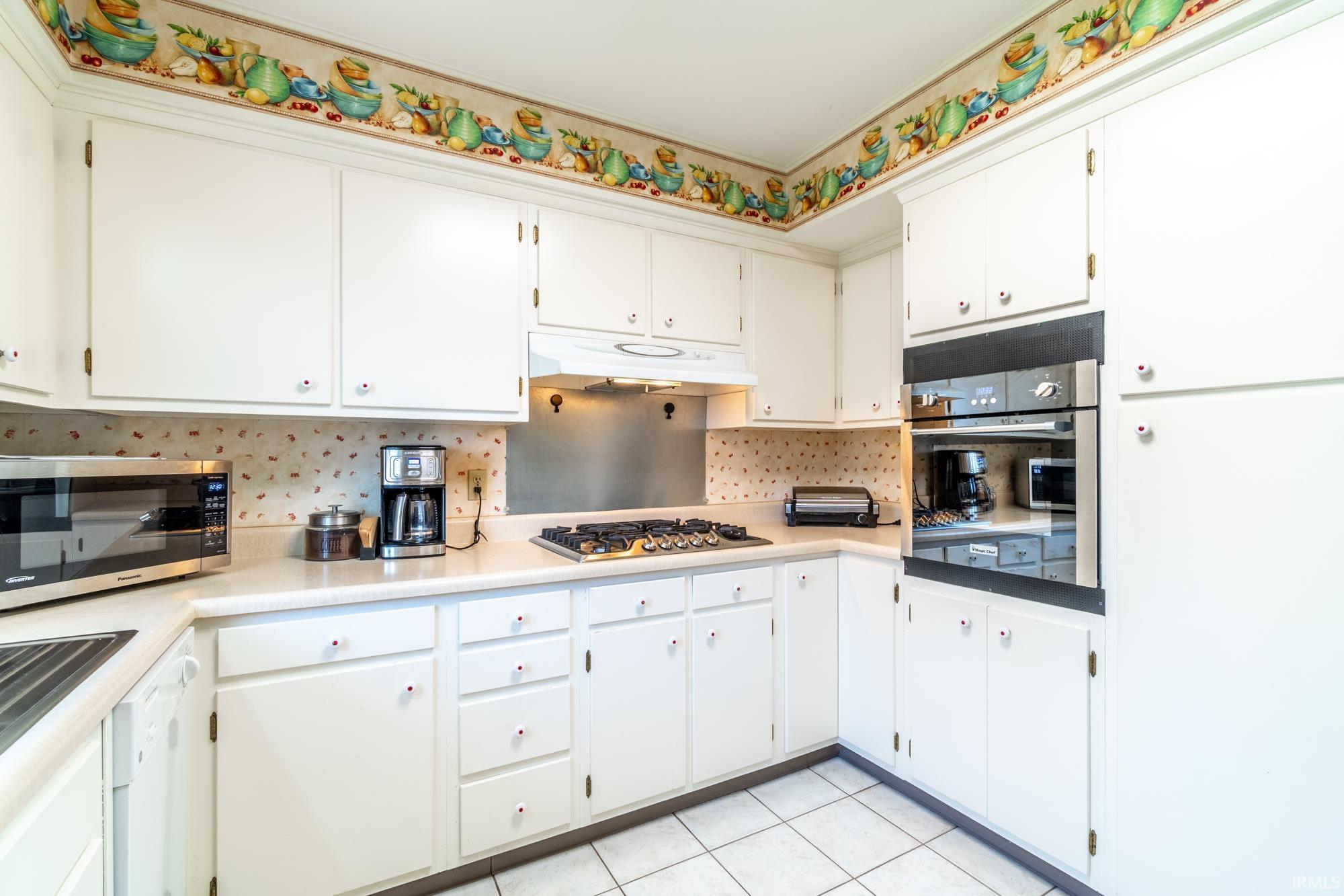 Kitchen featuring white cabinetry, light-toned countertops, a built-in wall oven, a gas cooktop, and tile flooring
