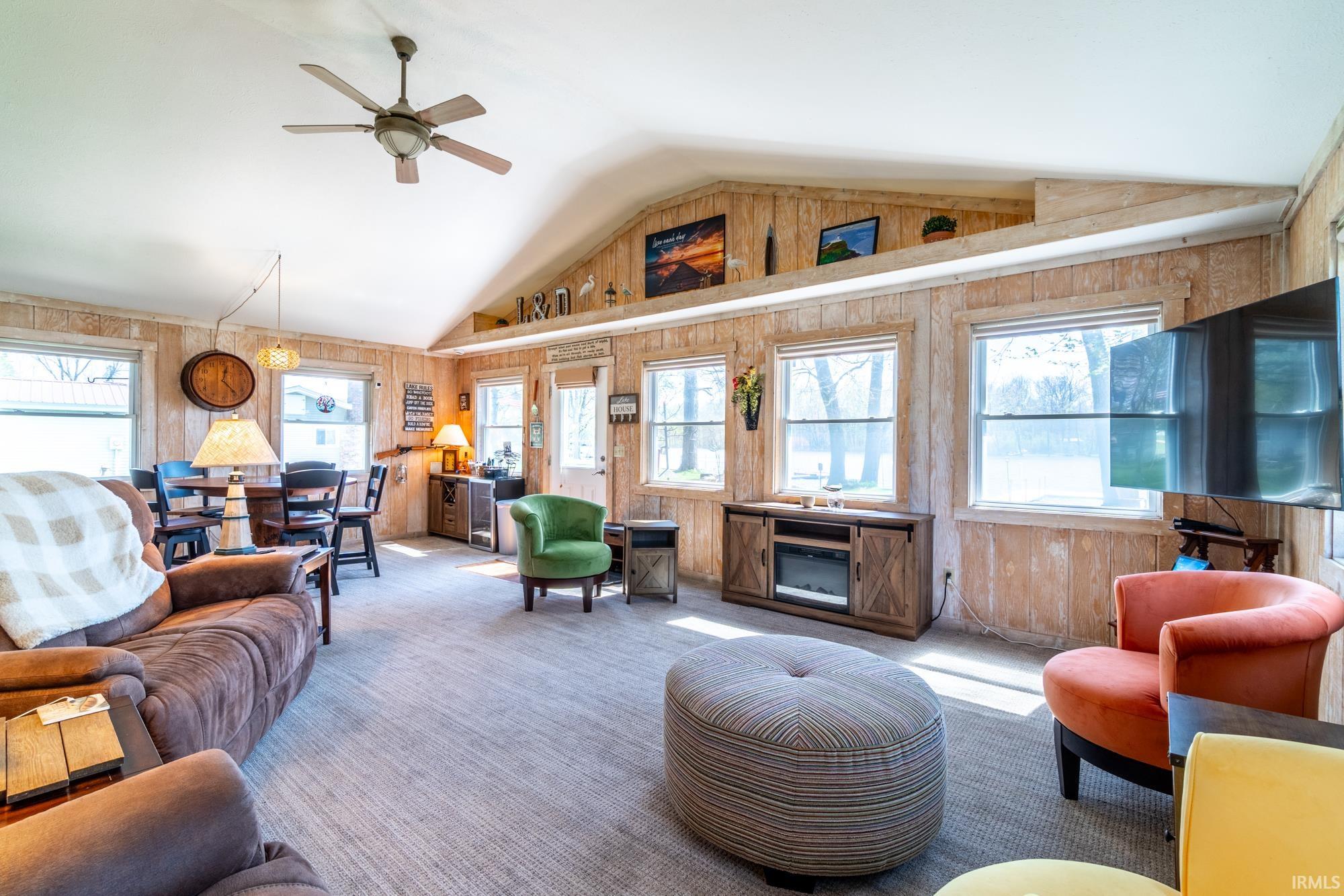 Spacious living area featuring a vaulted ceiling with a ceiling fan, light wood-finish wall panels, and multiple windows