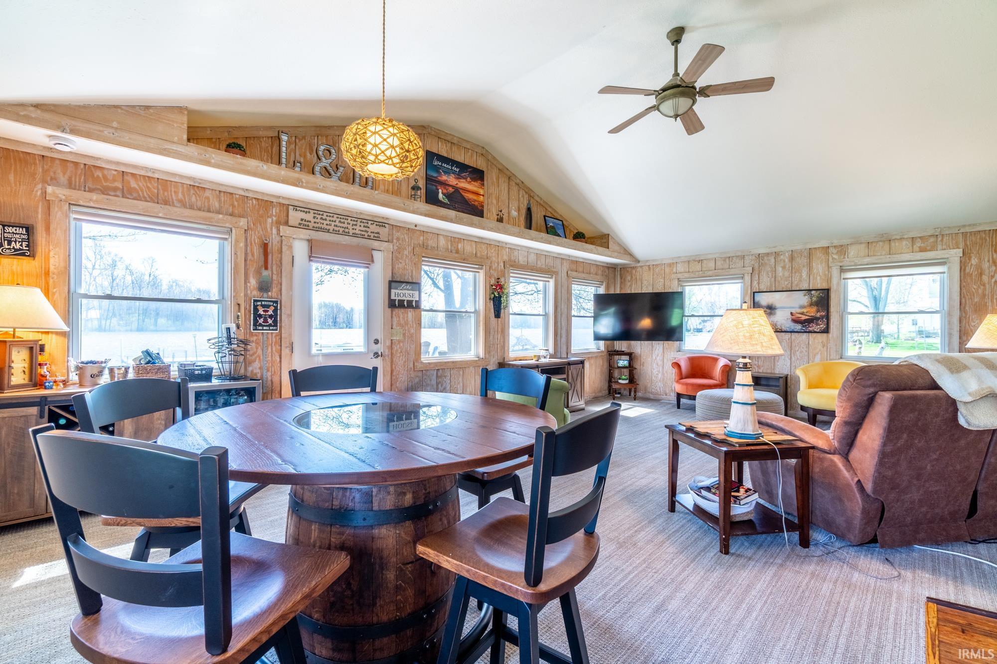 Vaulted ceiling living area featuring wood-paneled walls and multiple windows