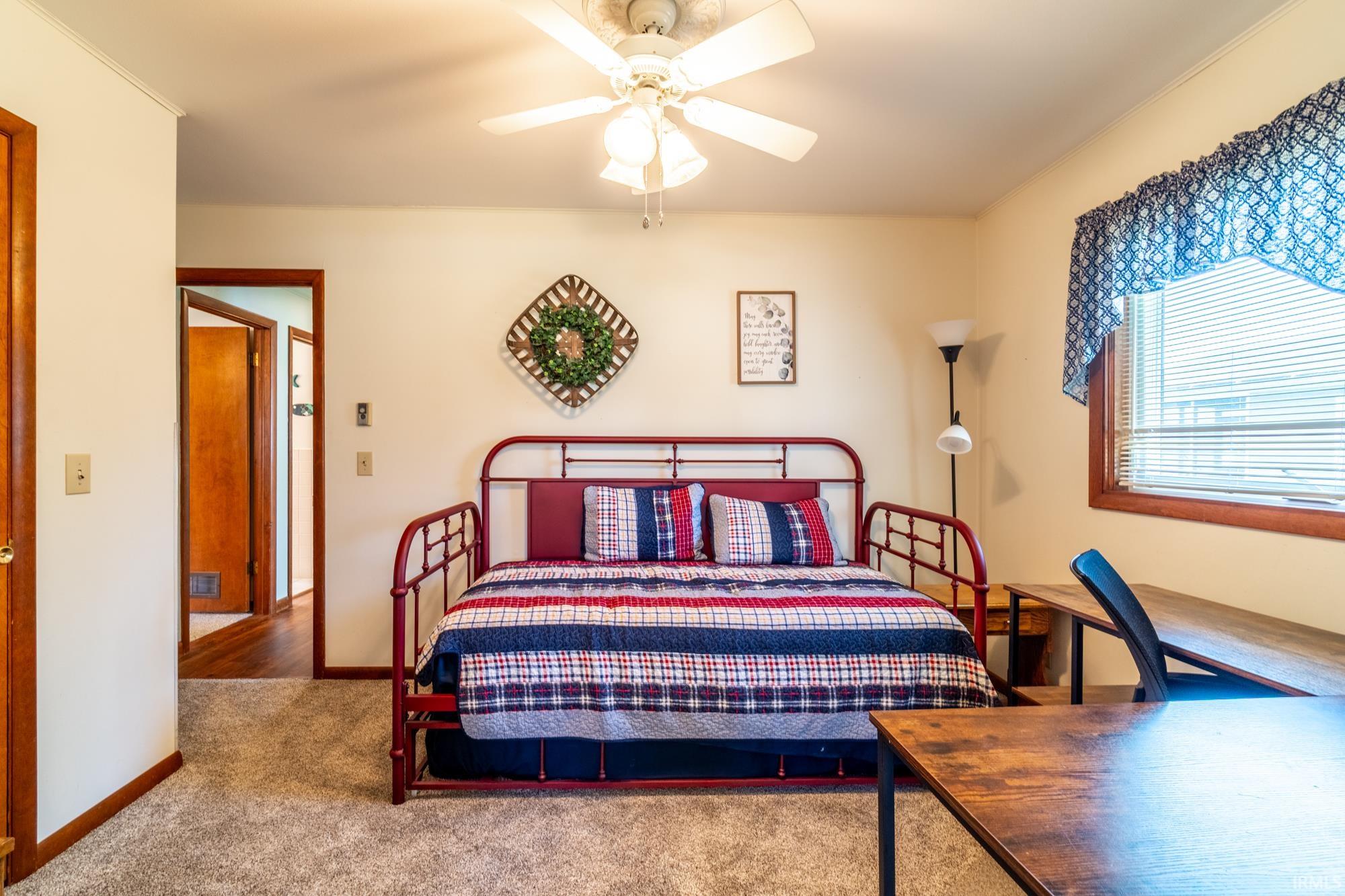 Carpeted room featuring a ceiling fan with light, a window with blinds, and wood-finish trim and doors