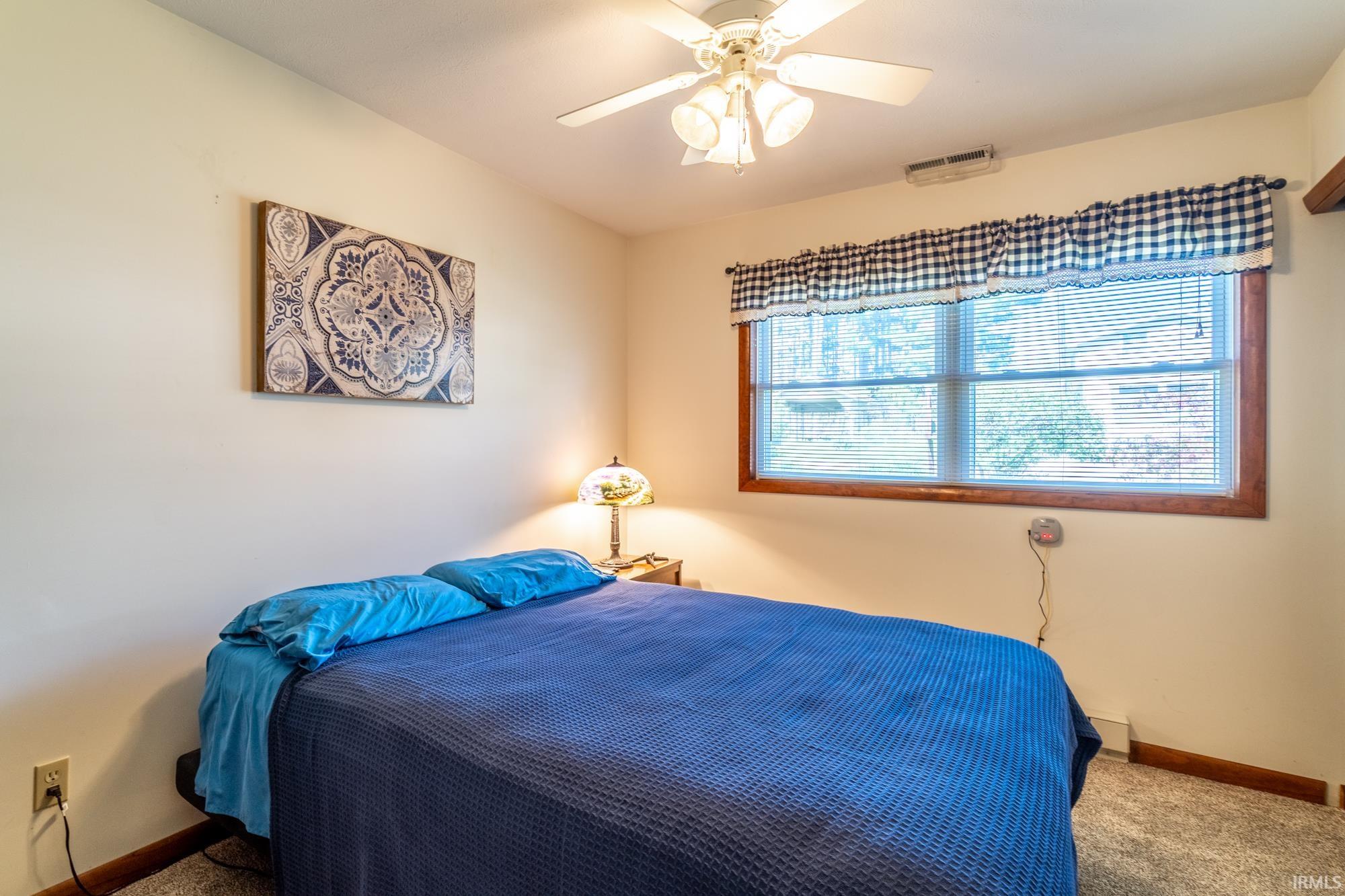Bedroom featuring a ceiling fan with integrated lighting, a window with wood trim, and textured carpeting