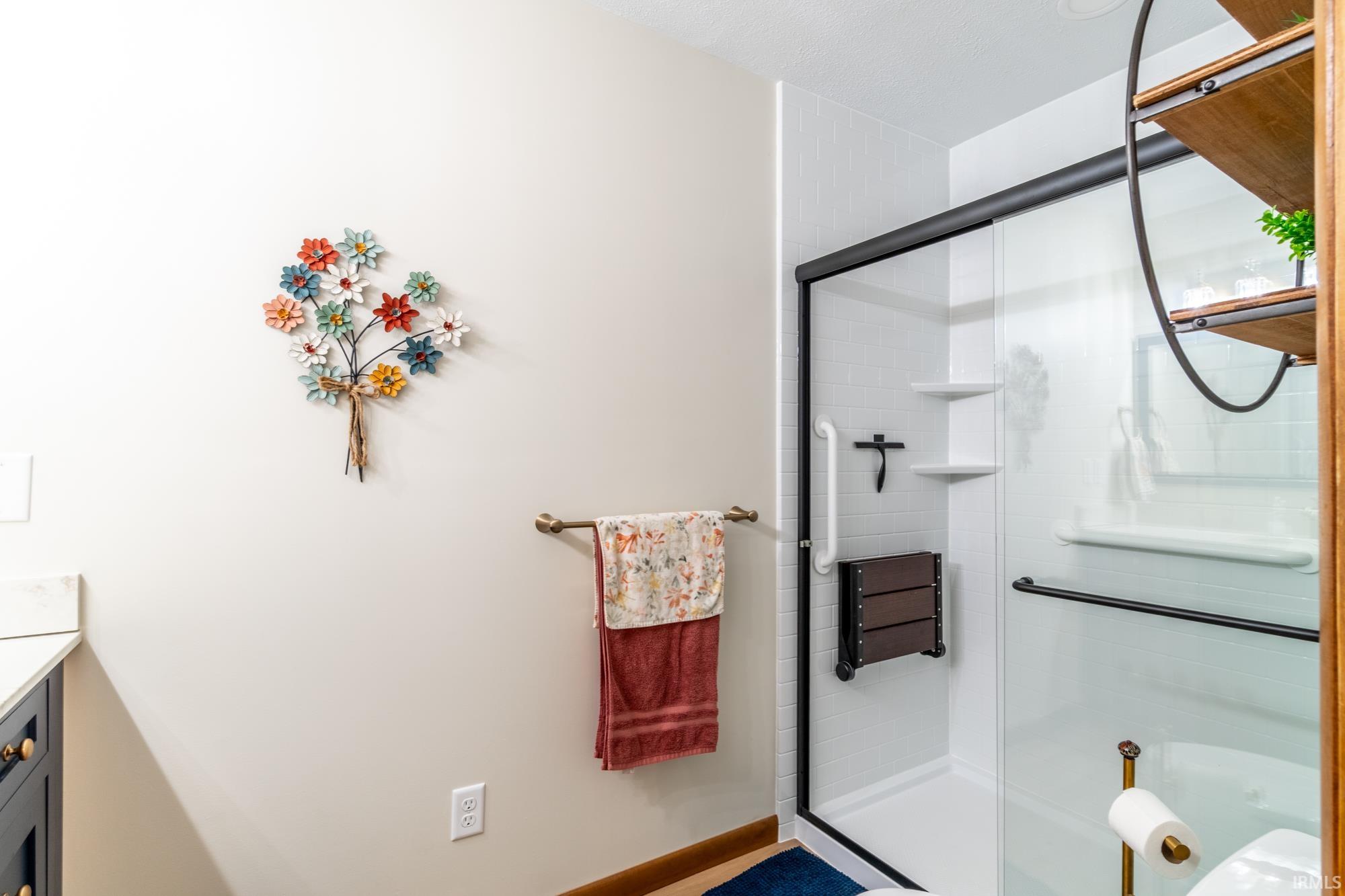 Shower enclosure with a black frame and clear glass door, featuring a white subway tile surround, integrated shelving, and a built-in folding shower seat