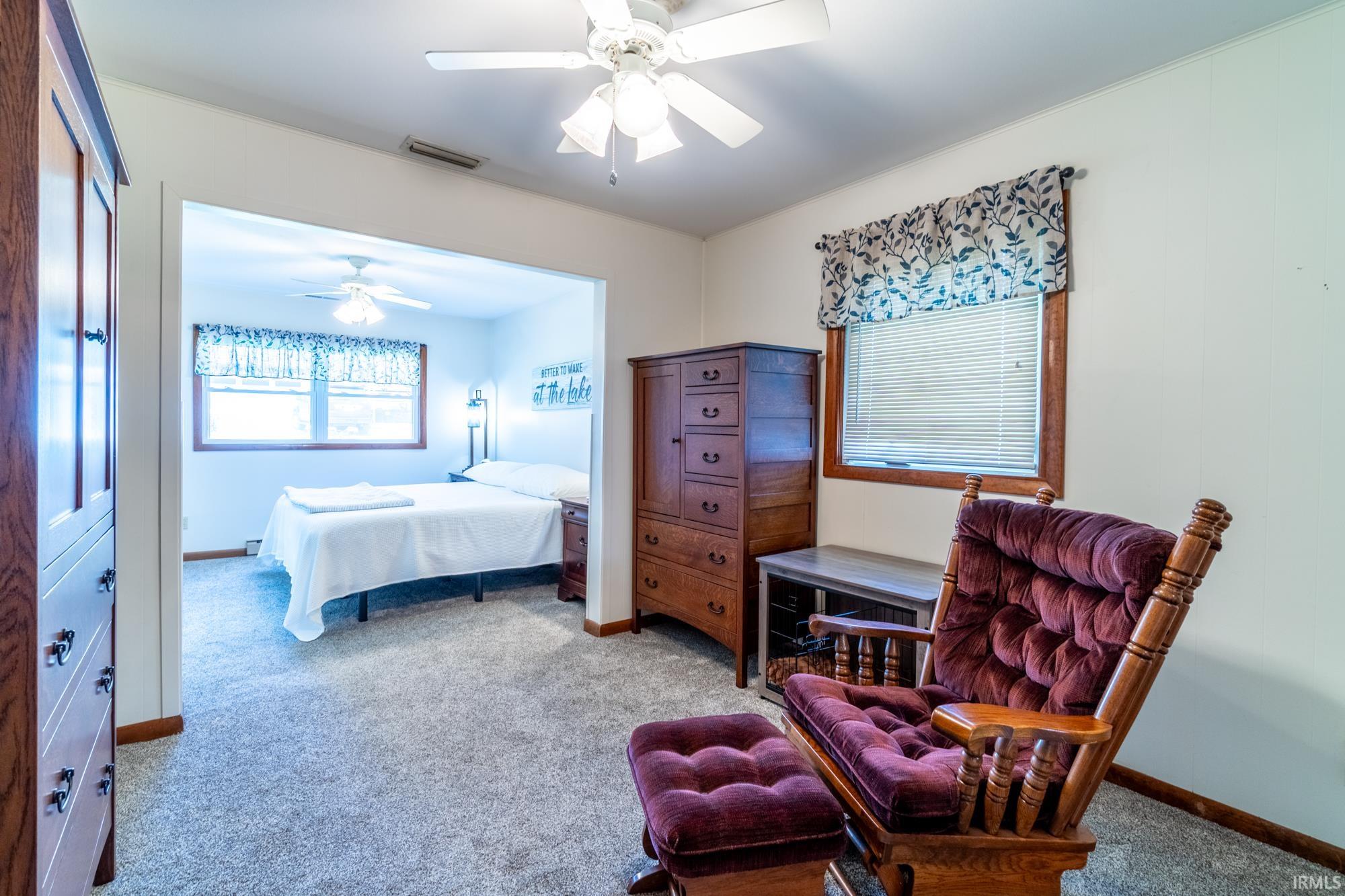 Carpeted bedroom area featuring a ceiling fan, a window with blinds, and a built-in architectural opening to an additional room with a ceiling fan and a window