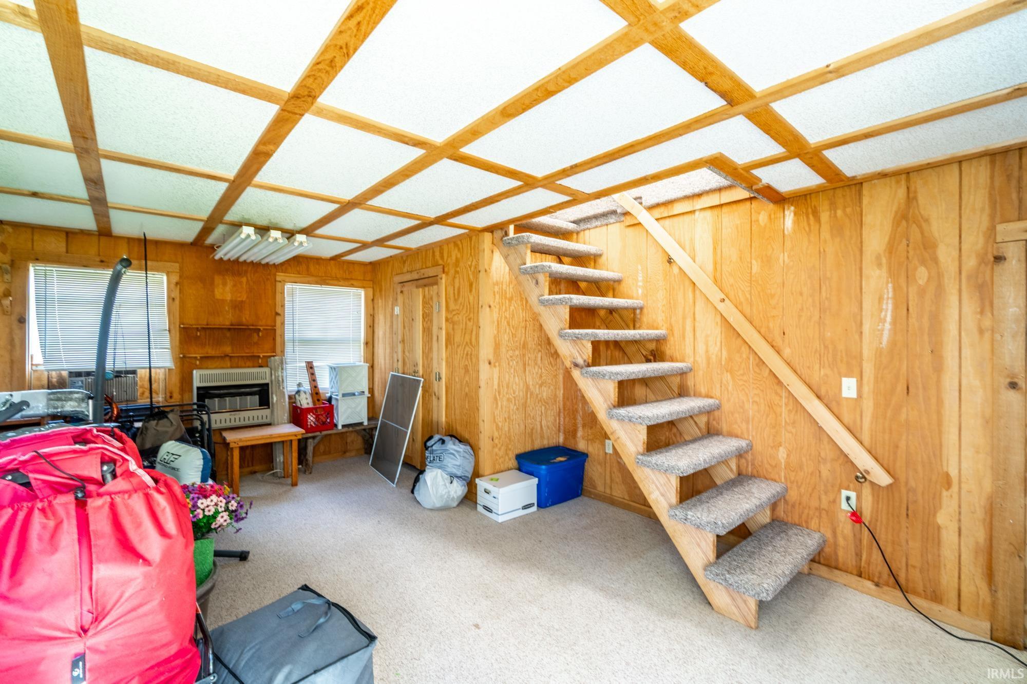 Interior space featuring wood paneling, carpeted flooring, and an exposed wood beam ceiling with white panels