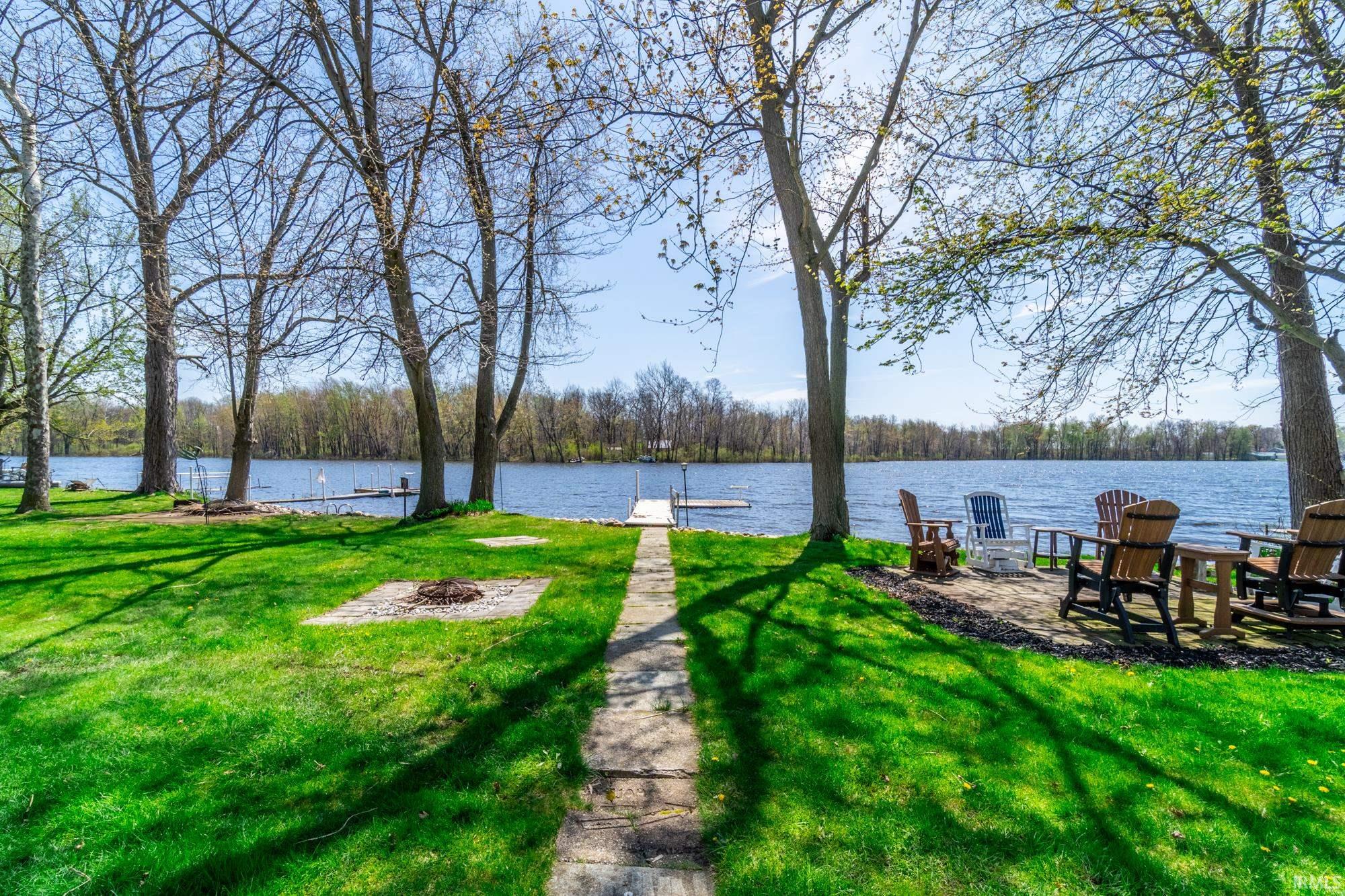 Manicured lawn bordered by mature trees, featuring a stone pathway leading to a permanent dock structure on the water