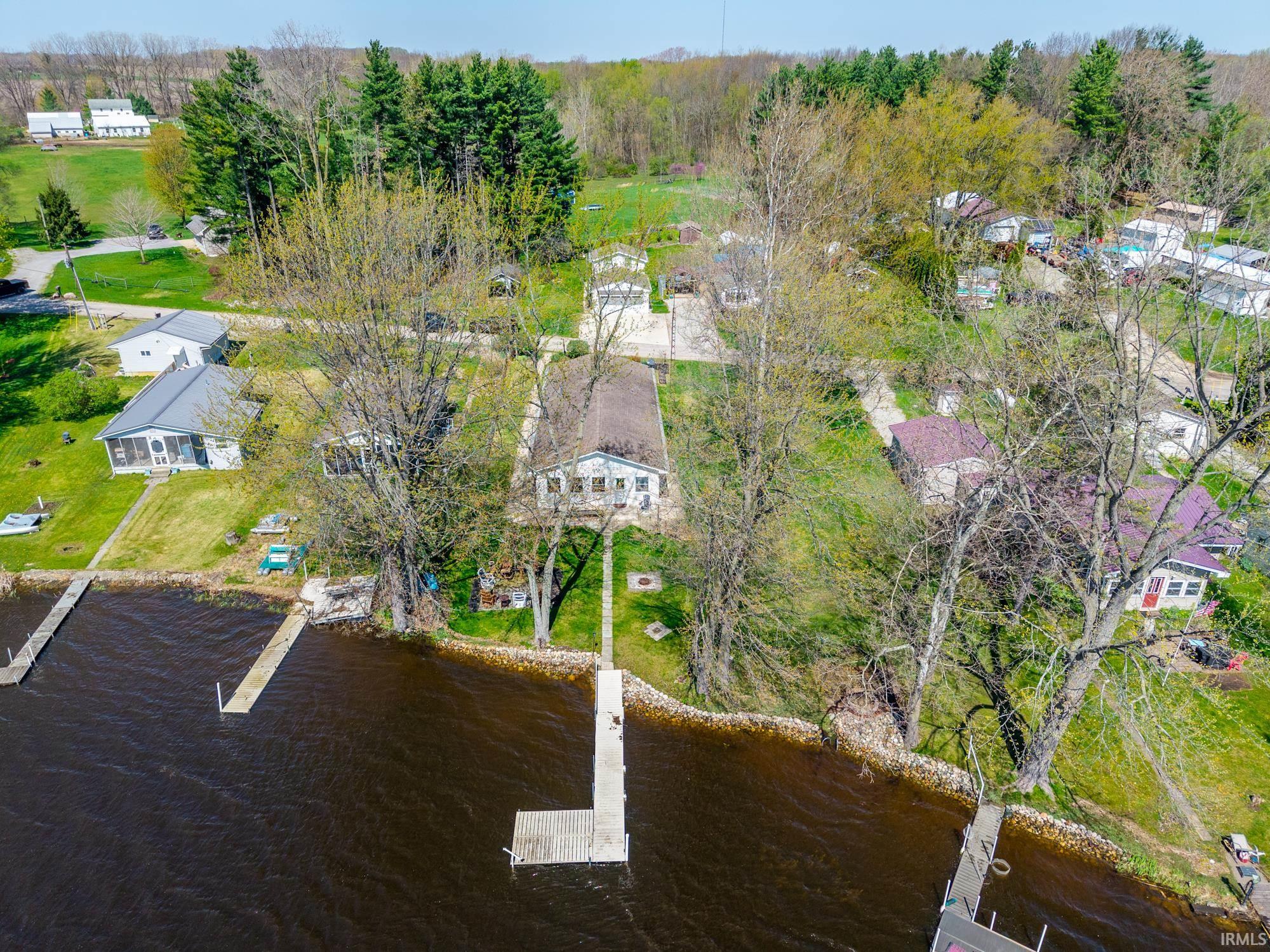 Waterfront property featuring a private dock, direct water access, a lush green lawn, mature trees, and a residential setting
