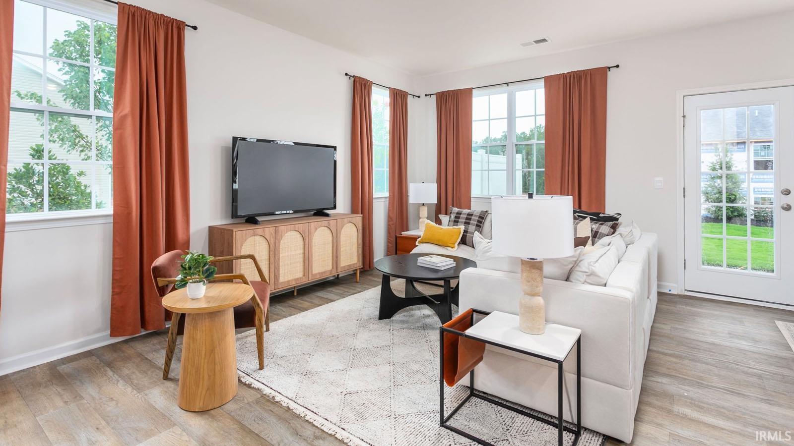 Living area with wood-finish flooring, multiple windows, a glass-paneled door, and white baseboards