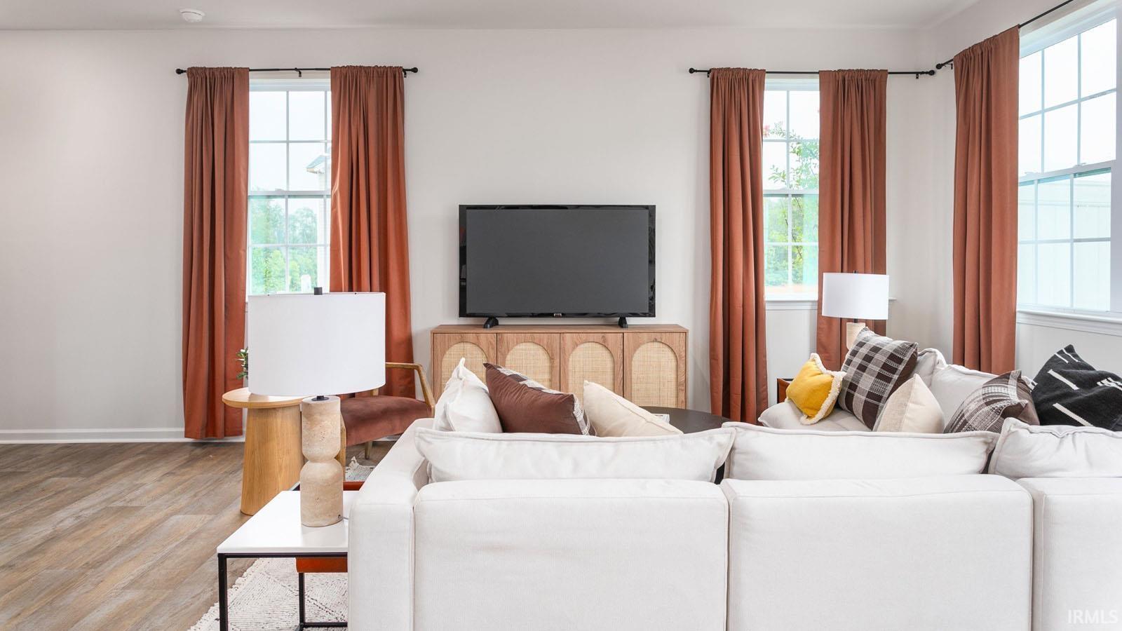 Spacious living area featuring expansive wood-finish flooring, multiple large windows providing ample natural light, and a built-in media console with storage