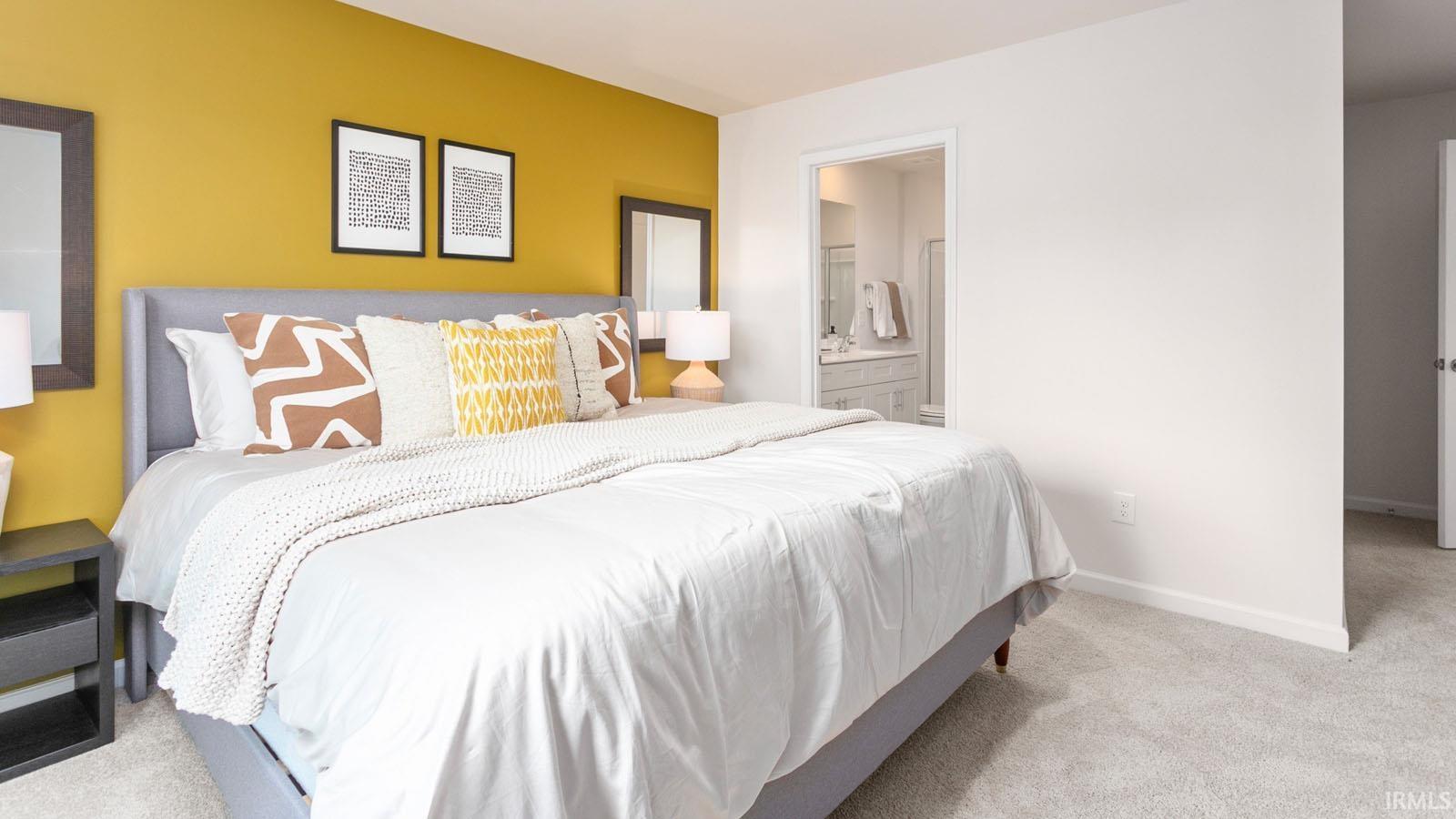 Carpeted bedroom featuring a contrasting accent wall, an open doorway to a bathroom with a vanity, and a second doorway