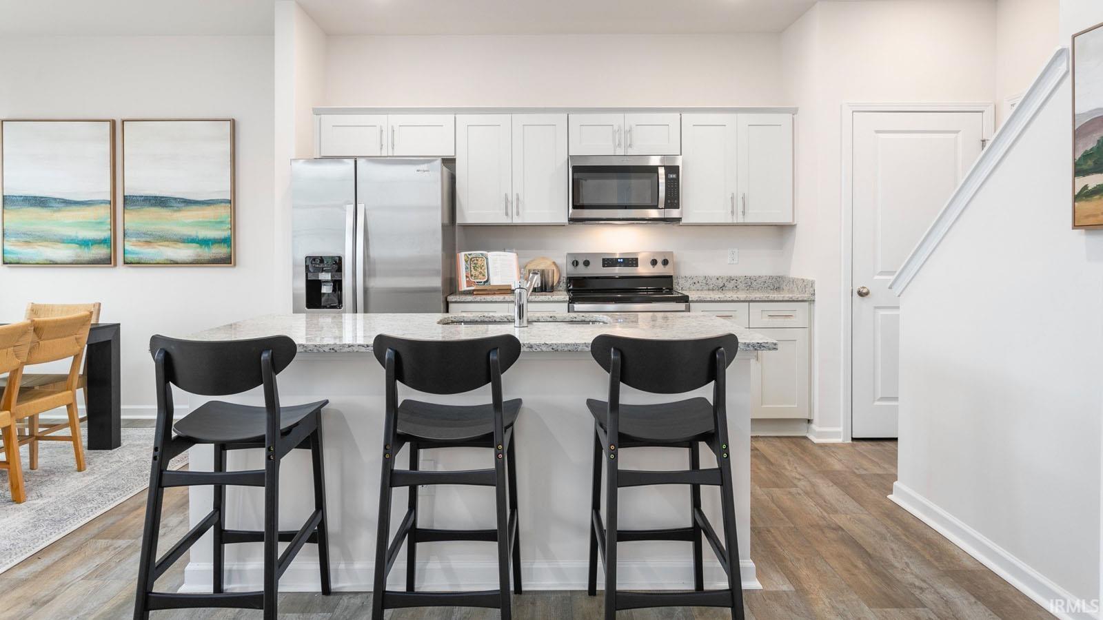 Contemporary kitchen featuring a breakfast bar with granite countertops, stainless steel appliances, white cabinetry, and wood-finish flooring