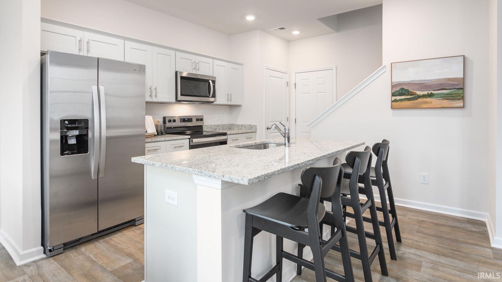 Kitchen featuring white cabinetry, stainless steel appliances, granite countertops, an undermount sink, and wood-finish flooring