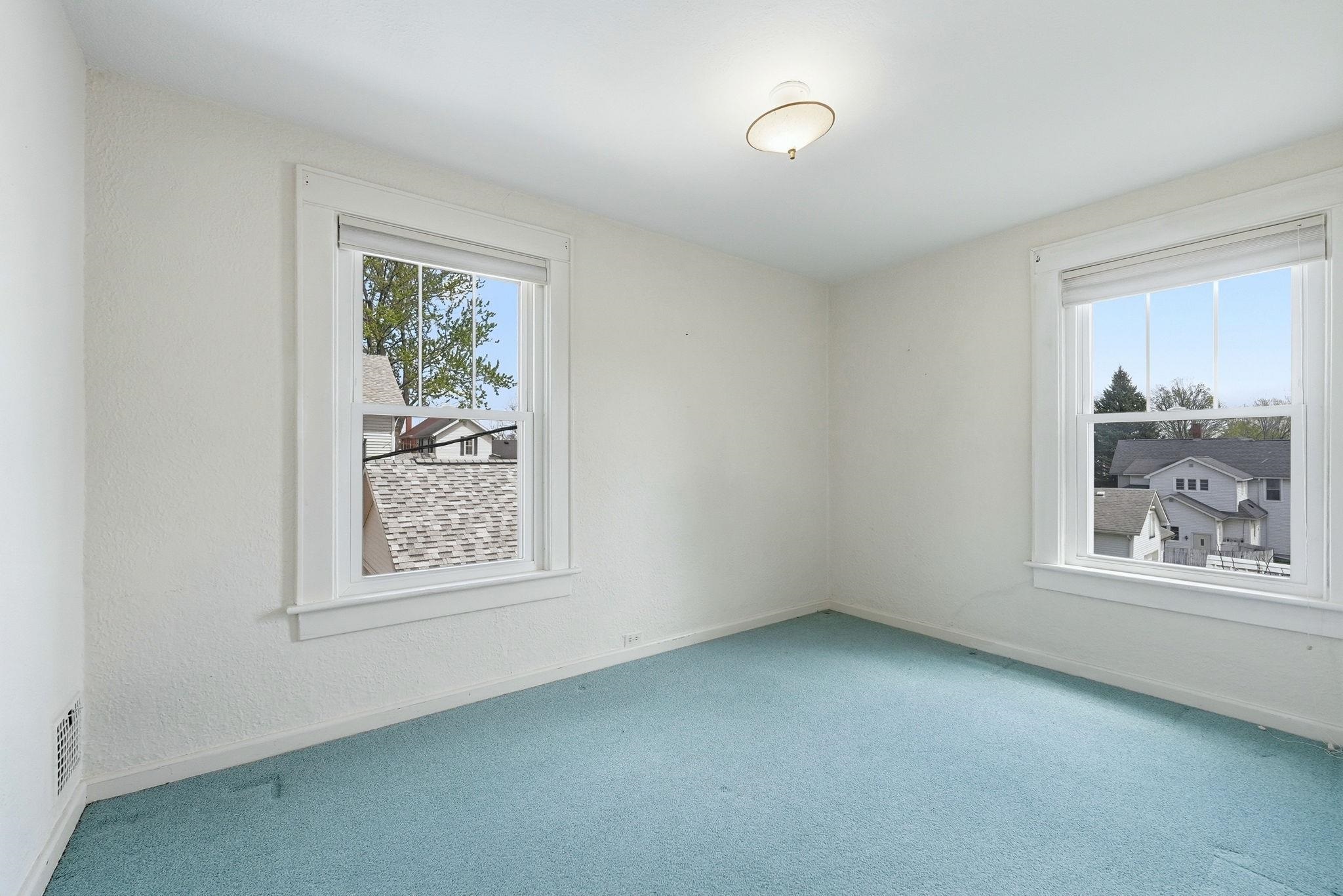 Bright room featuring two large windows with white trim, light blue carpeting, white walls, and a ceiling-mounted light fixture