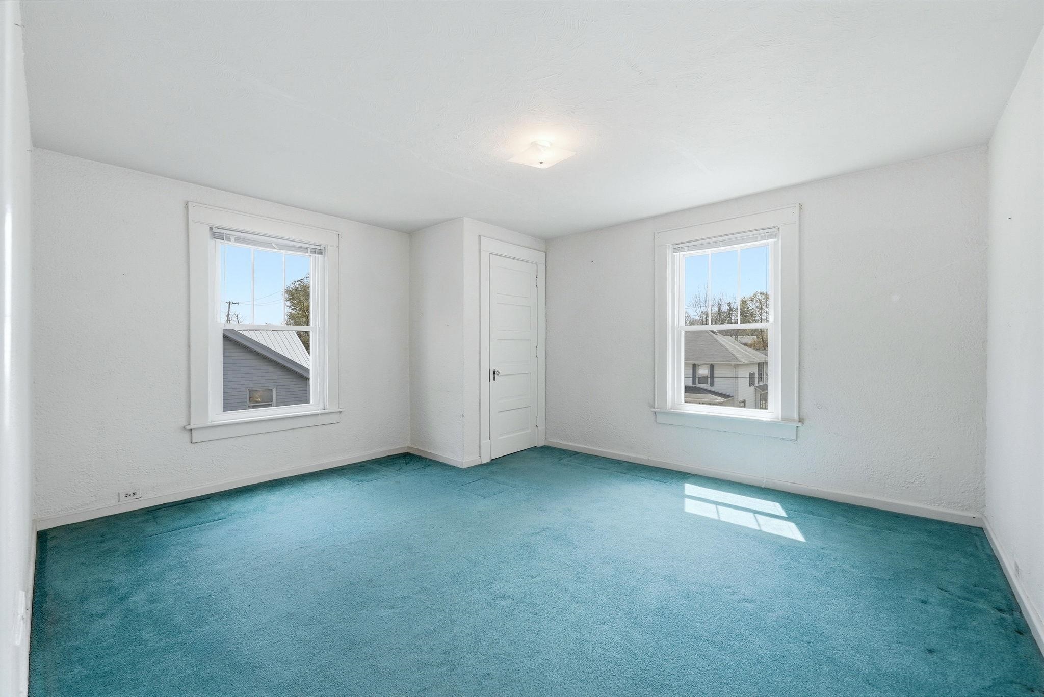 Room featuring two windows with white trim, a white paneled door, and teal carpeting