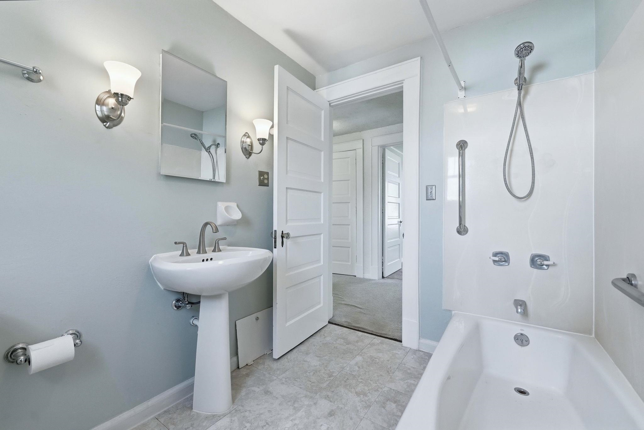 Bathroom featuring a white pedestal sink, brushed nickel fixtures, a tub-shower combination with a wall-mounted showerhead, and grab bars