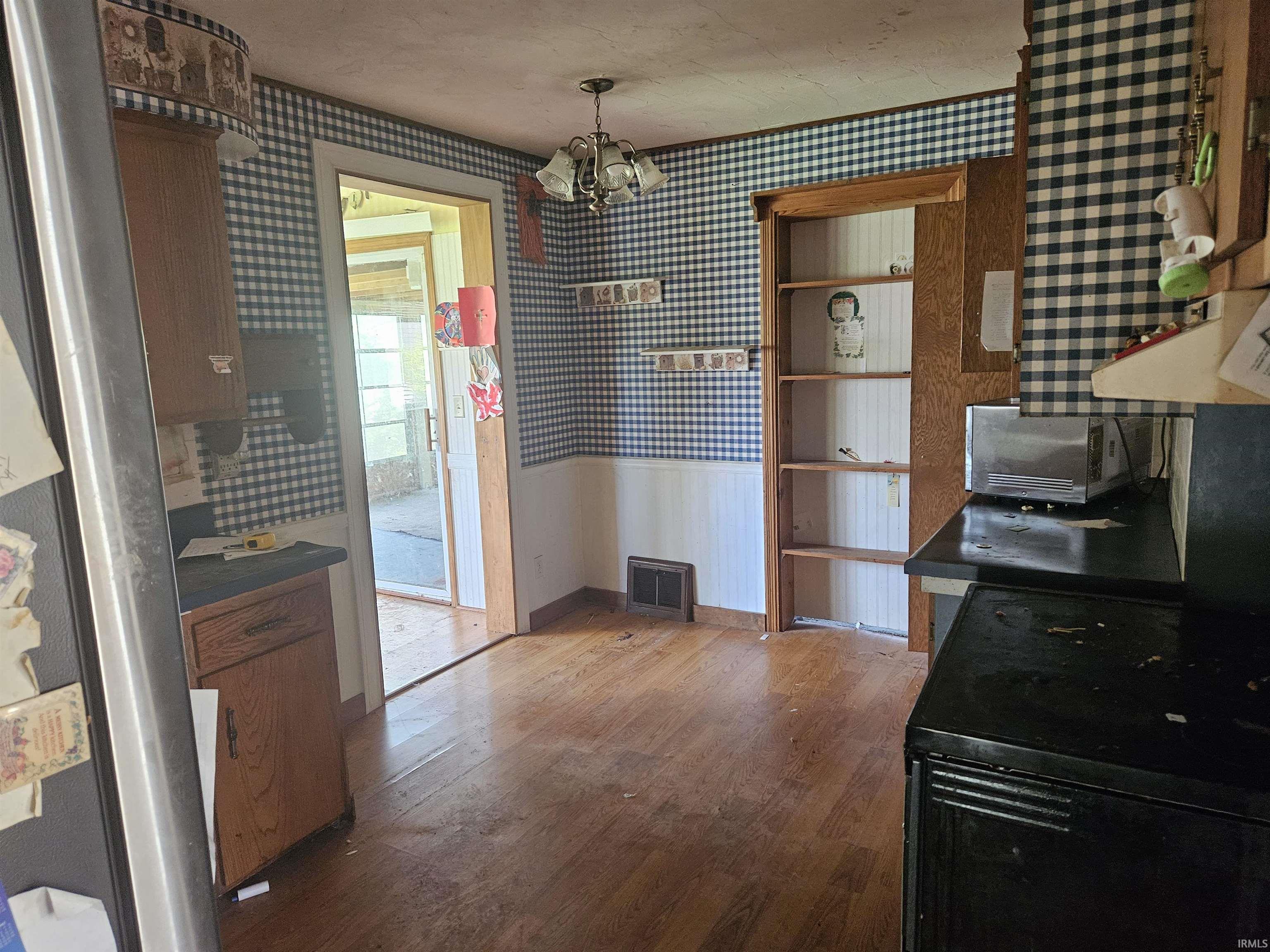 Kitchen featuring wood-finish flooring, built-in shelving, checkered wallpaper with wainscoting, and a ceiling-mounted light fixture