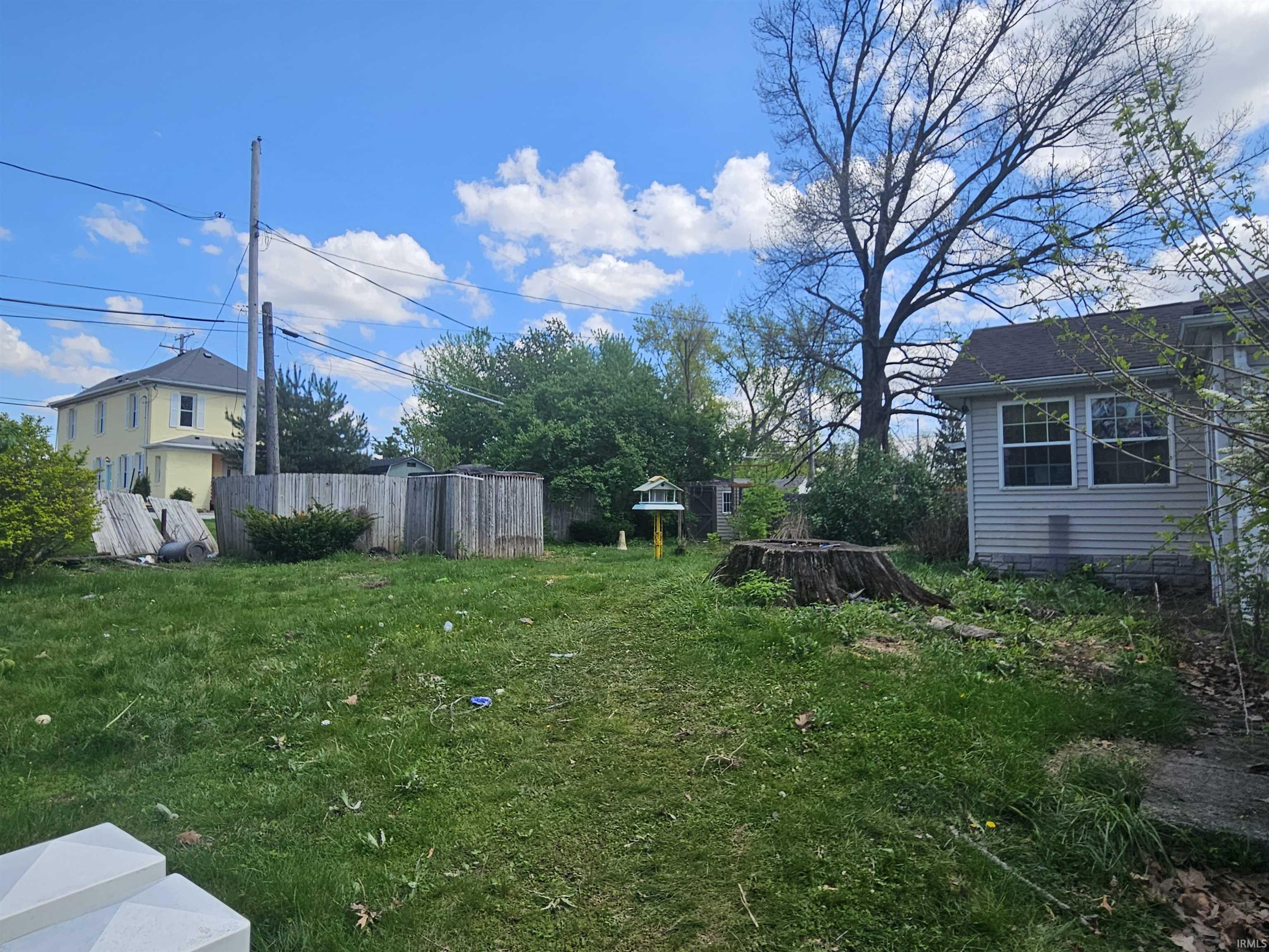 Expansive green lawn with mature trees and a partial wood fence