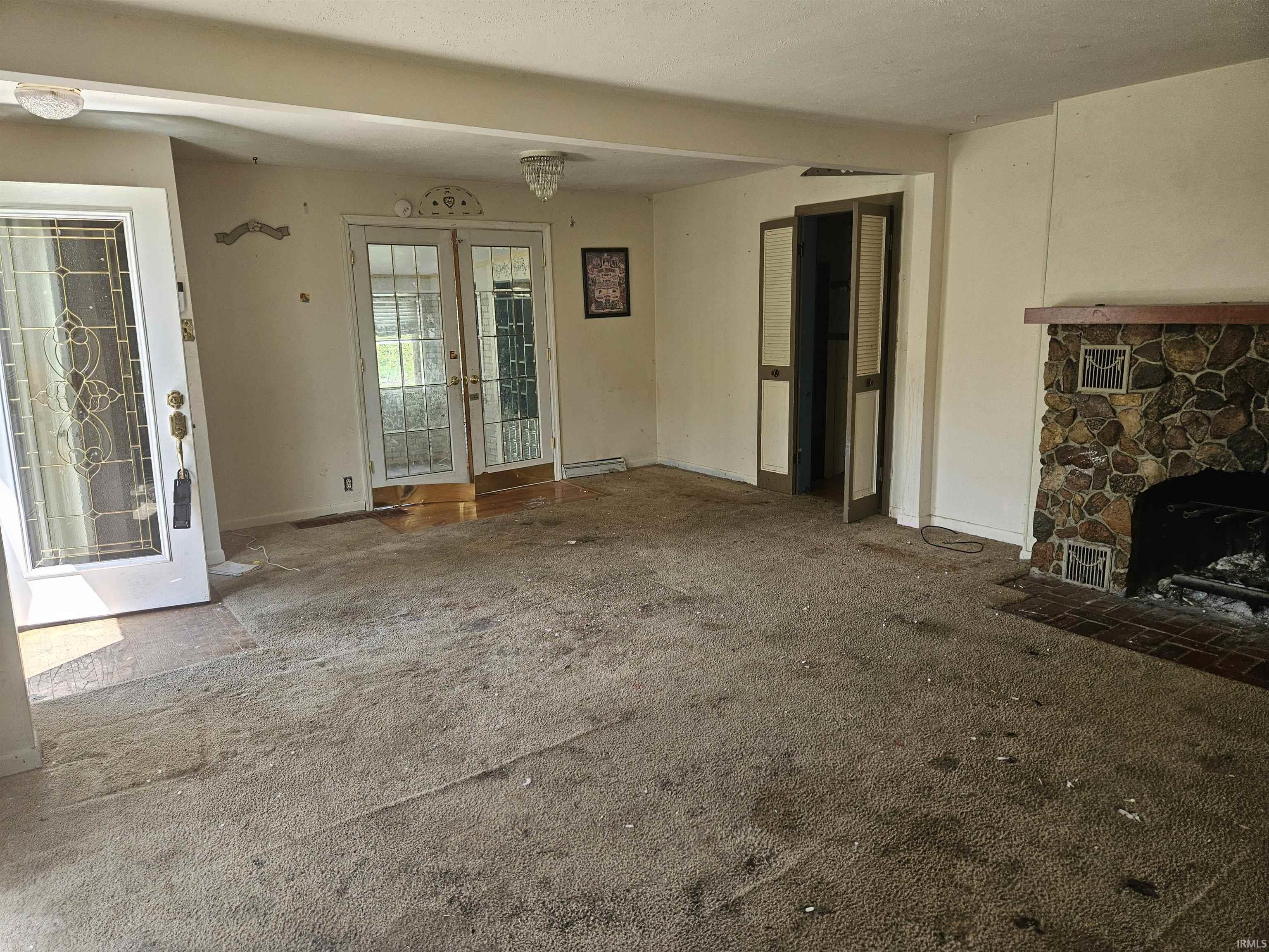 Living area featuring a stone fireplace with a wood mantle, double glass-paneled doors, and an additional glass-paneled entry door