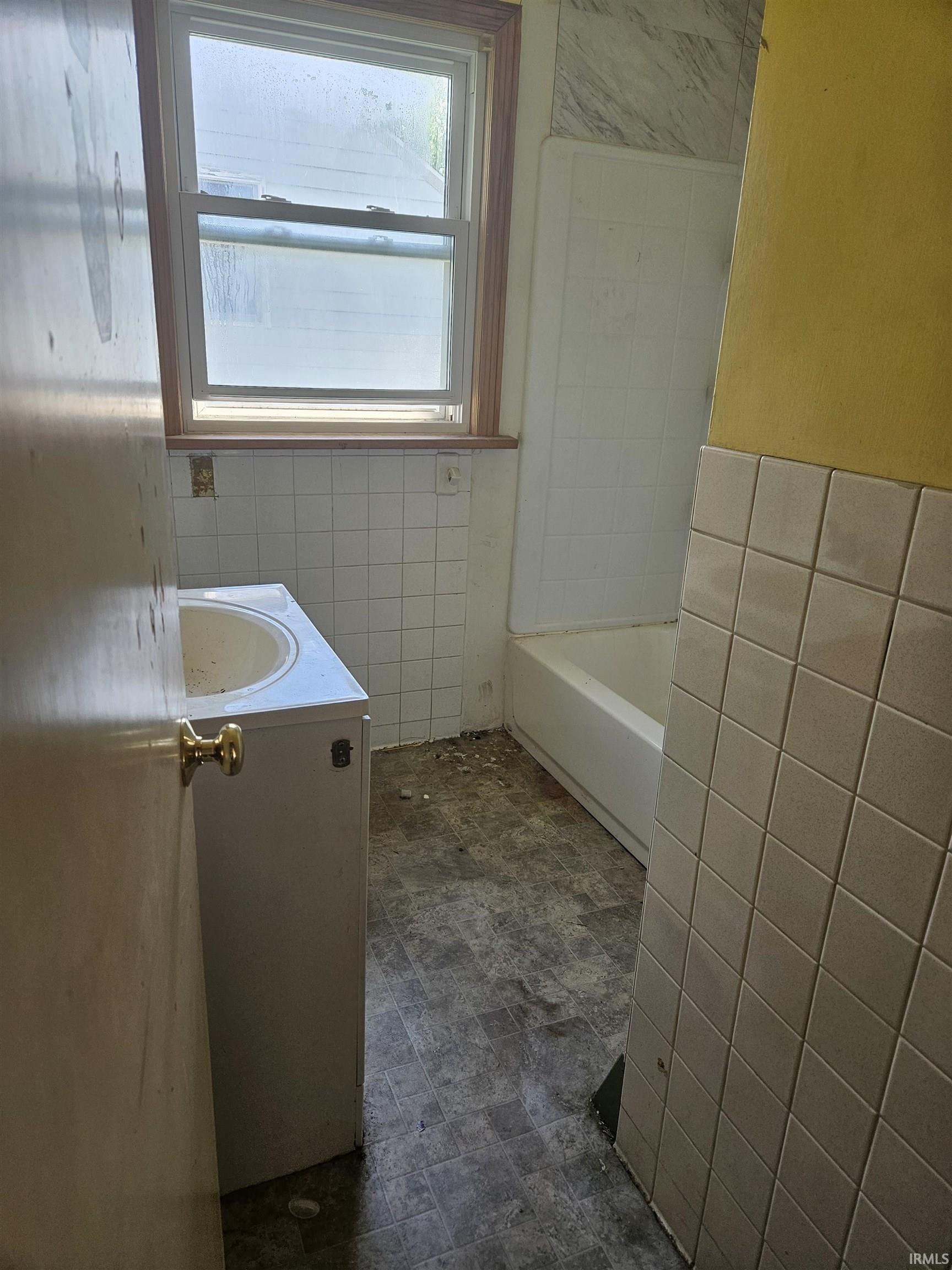Bathroom featuring a single-pane window with wood-finish trim, a white tile-surround bathtub, and a single vanity with an integrated sink
