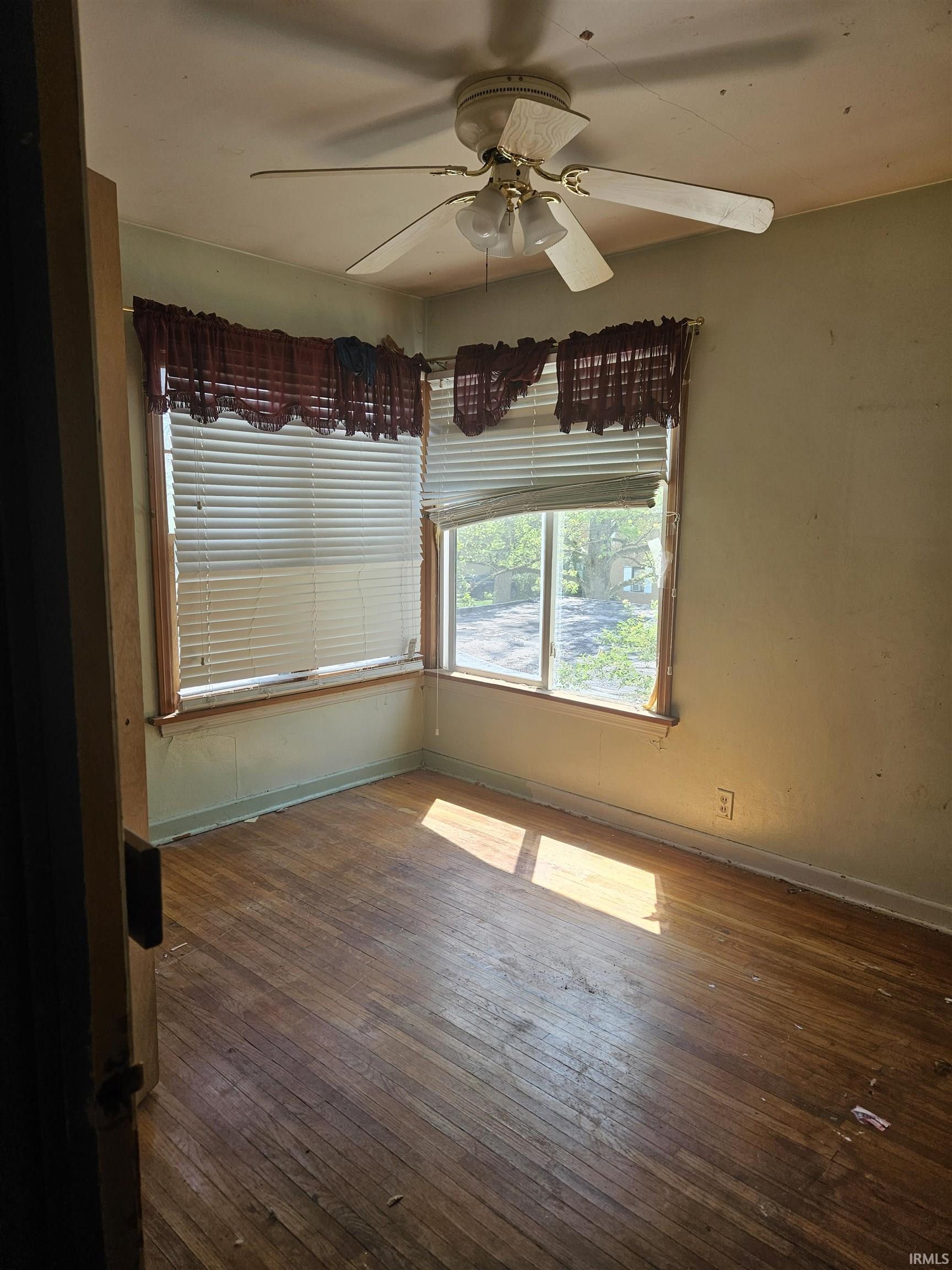 Room featuring wood-finish flooring, two windows, and a ceiling fan with integrated lighting