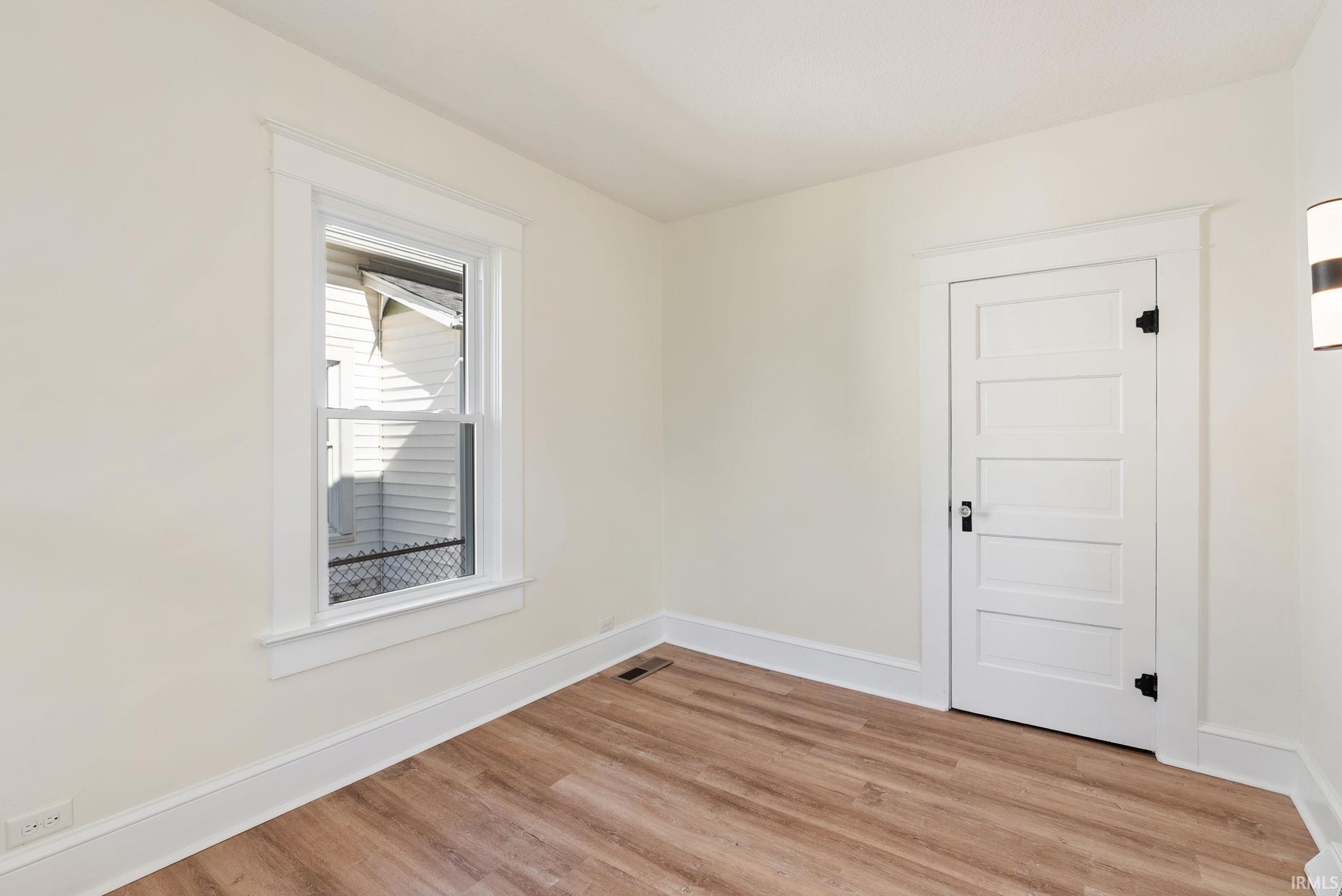 Interior room featuring wood-finish flooring, white trim, and a five-panel interior door with matte black hardware