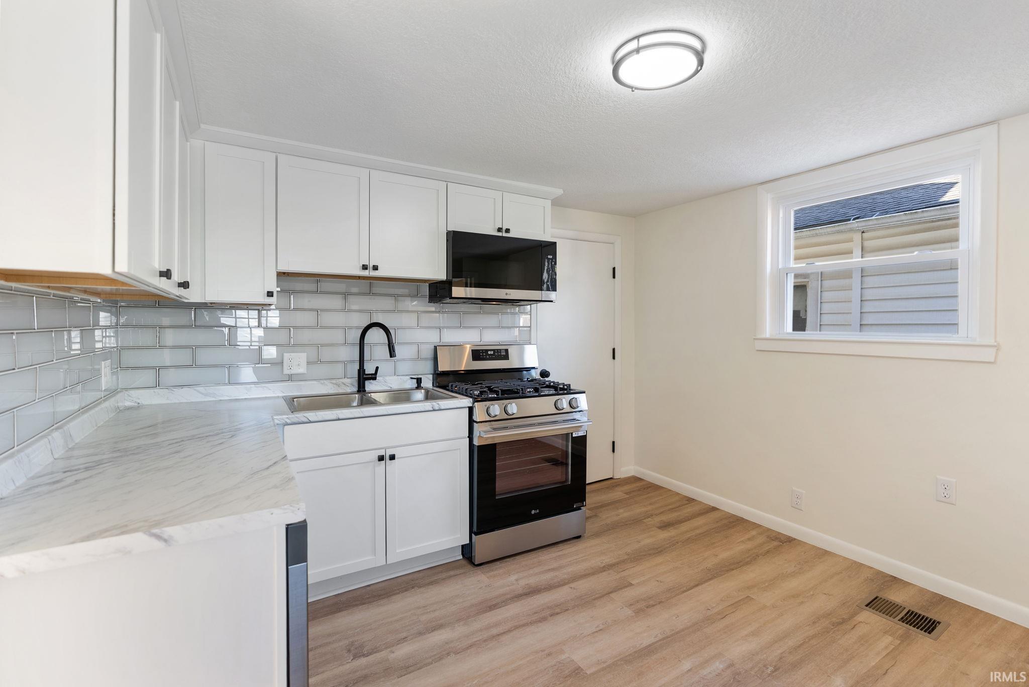 Contemporary kitchen featuring white cabinetry, a subway tile backsplash, light-toned countertops, stainless steel appliances, and wood-finish flooring