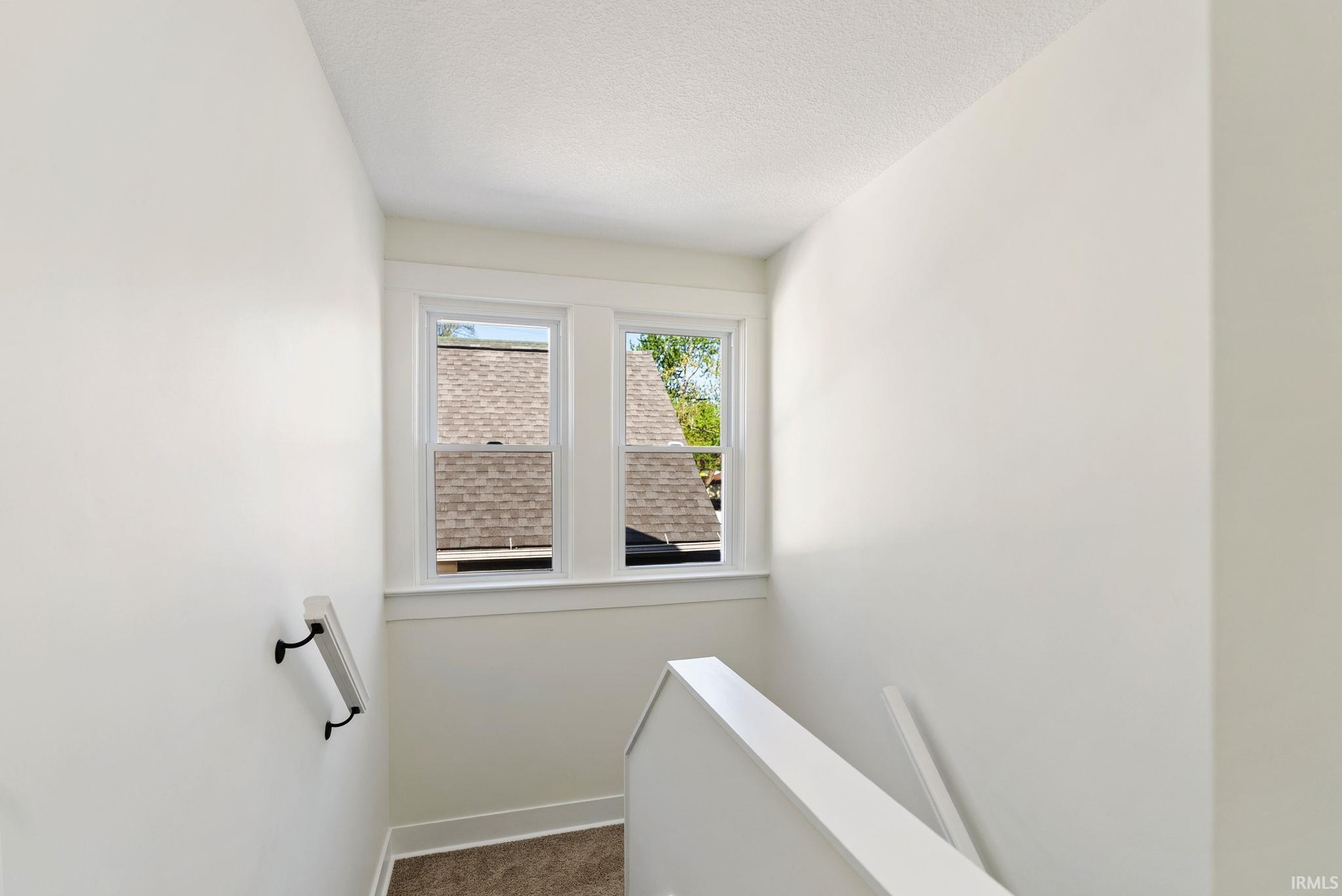 Stairwell featuring light neutral paint, white trim, dual windows, and a white handrail with black accents