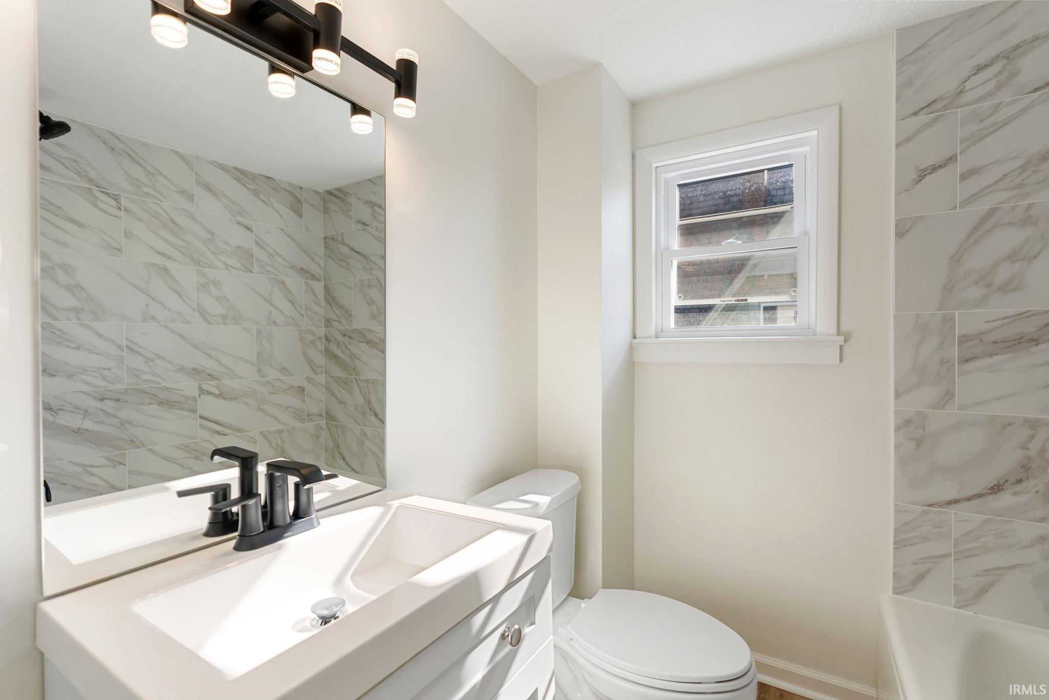 Bathroom featuring light-toned wall paint, a white vanity with integrated sink, black-finish faucet, and a large mirror